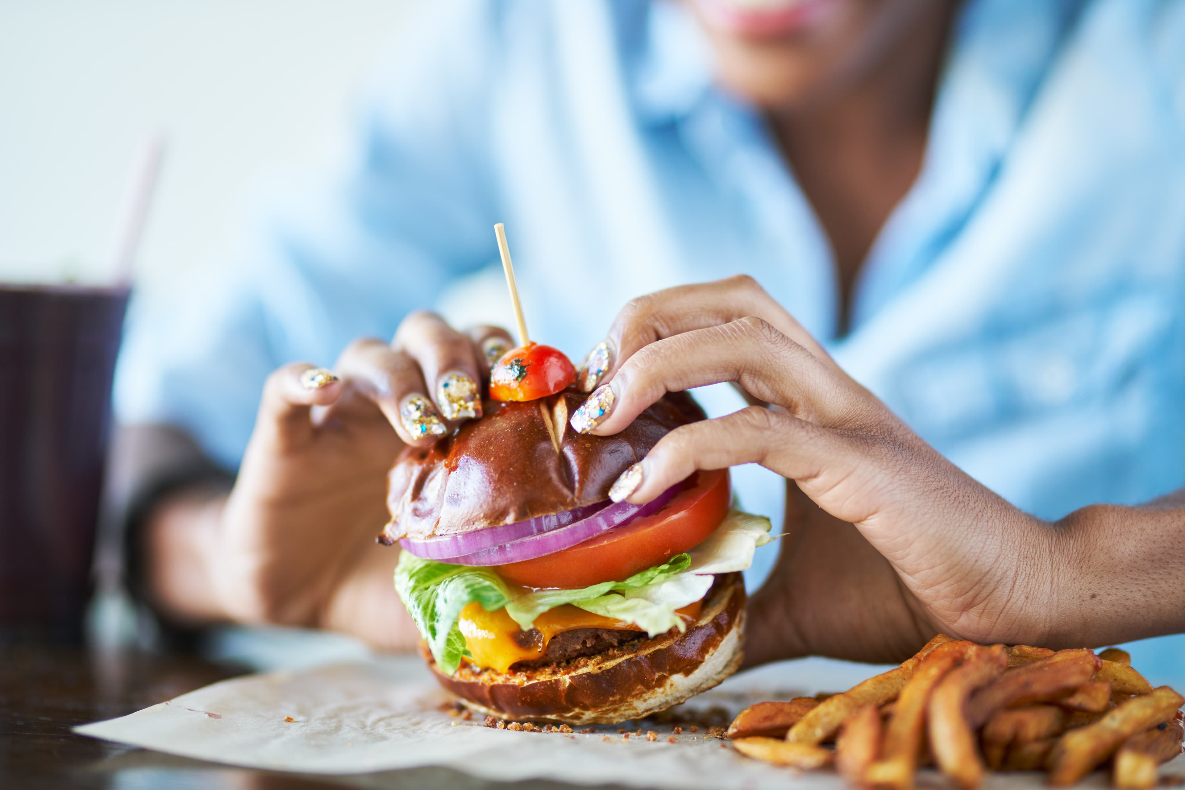 close up of african american woman about to eat vegan meatless cheese burger at restaurant close up of african american woman about to eat vegan meatless cheese burger at restaurant
