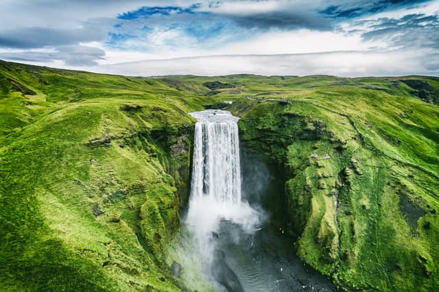 Iceland waterfall Skogafoss in Icelandic nature landscape. Famous tourist attractions and landmarks destination in Icelandic nature landscape on South Iceland. Aerial drone view of top waterfall. Iceland waterfall Skogafoss in Icelandic nature landscape. Famous tourist attractions and landmarks destination in Icelandic nature landscape on South Iceland. Aerial drone view of top waterfall.