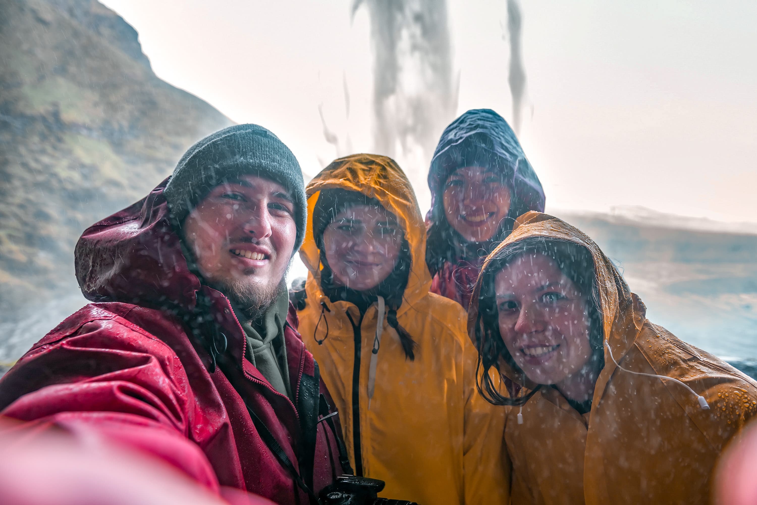 four friends in raincoats make a selfie under an Icelandic waterfall Seljalandsfoss four friends make a selfie under an Icelandic waterfall