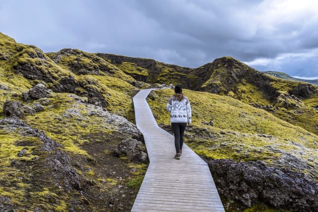 Girl teenager is following wooden foot pass to the crater Tjarnargigur in Lakagigar volcanic fissure area in Southern highlands of Iceland. Girl teenager is following wooden foot pass to the crater Tjarnargigur in Lakagigar volcanic fissure area in Southern highlands of Iceland
