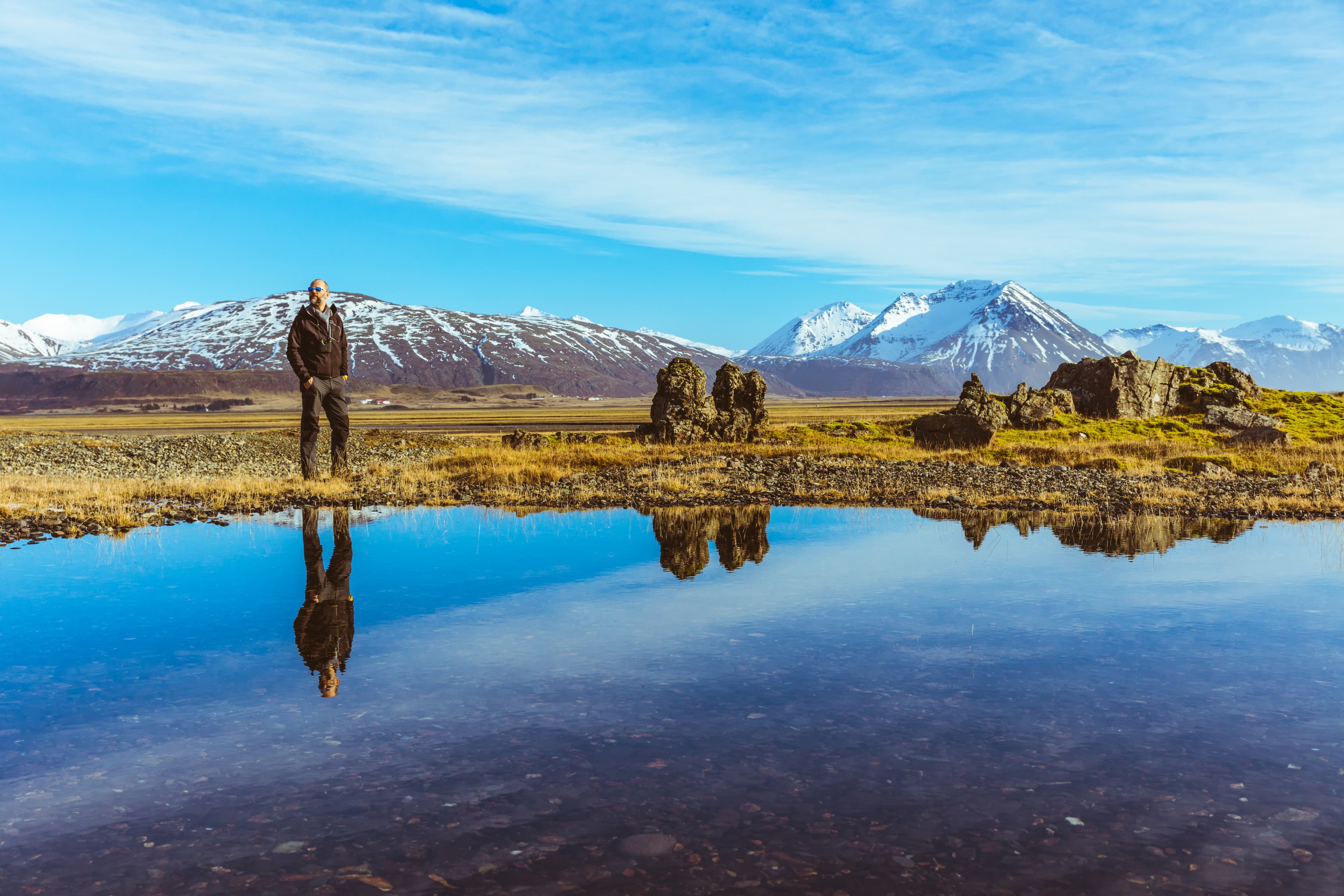 Man explorer in Iceland with his reflection on the water. Adult man walking and looking around. Majestic mountains on background, reflections on water on foreground. Travel and wanderlust concept Man explorer in Iceland with his reflection on the water