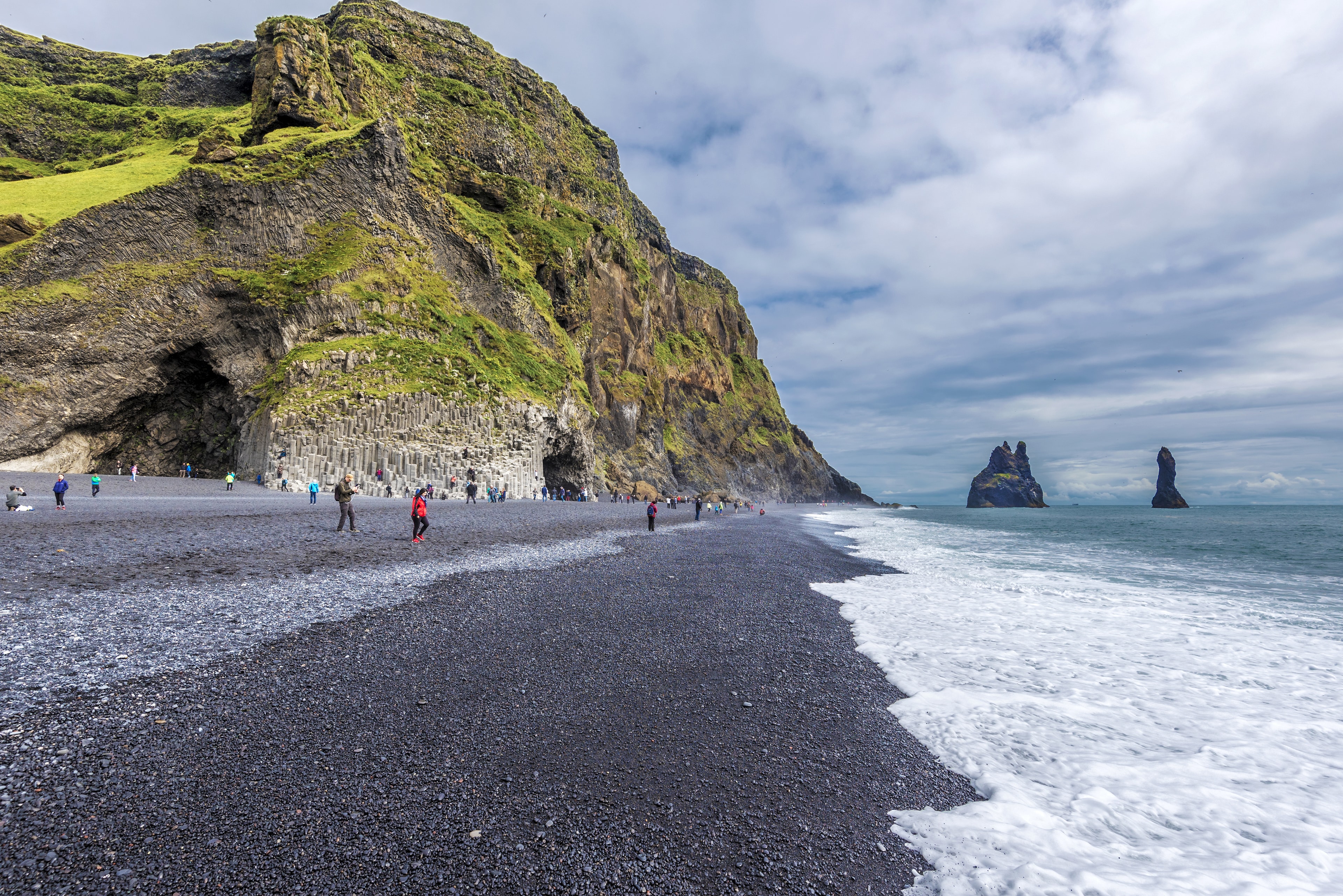 Vik I Myrdal,  Iceland – 23 July, 2018 View at Reynisfjara  black sand beach in Southern Iceland. Reynisfjall mountain and Gardar basalt columns are at left and Reynisdrangar  basalt sea stacks are at right background. View at Reynisfjara  black sand beach in Southern Iceland. Reynisfjall mountain and Gardar basalt columns are at left and Reynisdrangar  basalt sea stacks are at right background.