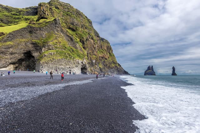 Vik I Myrdal,  Iceland – 23 July, 2018 View at Reynisfjara  black sand beach in Southern Iceland. Reynisfjall mountain and Gardar basalt columns are at left and Reynisdrangar  basalt sea stacks are at right background. View at Reynisfjara  black sand beach in Southern Iceland. Reynisfjall mountain and Gardar basalt columns are at left and Reynisdrangar  basalt sea stacks are at right background.