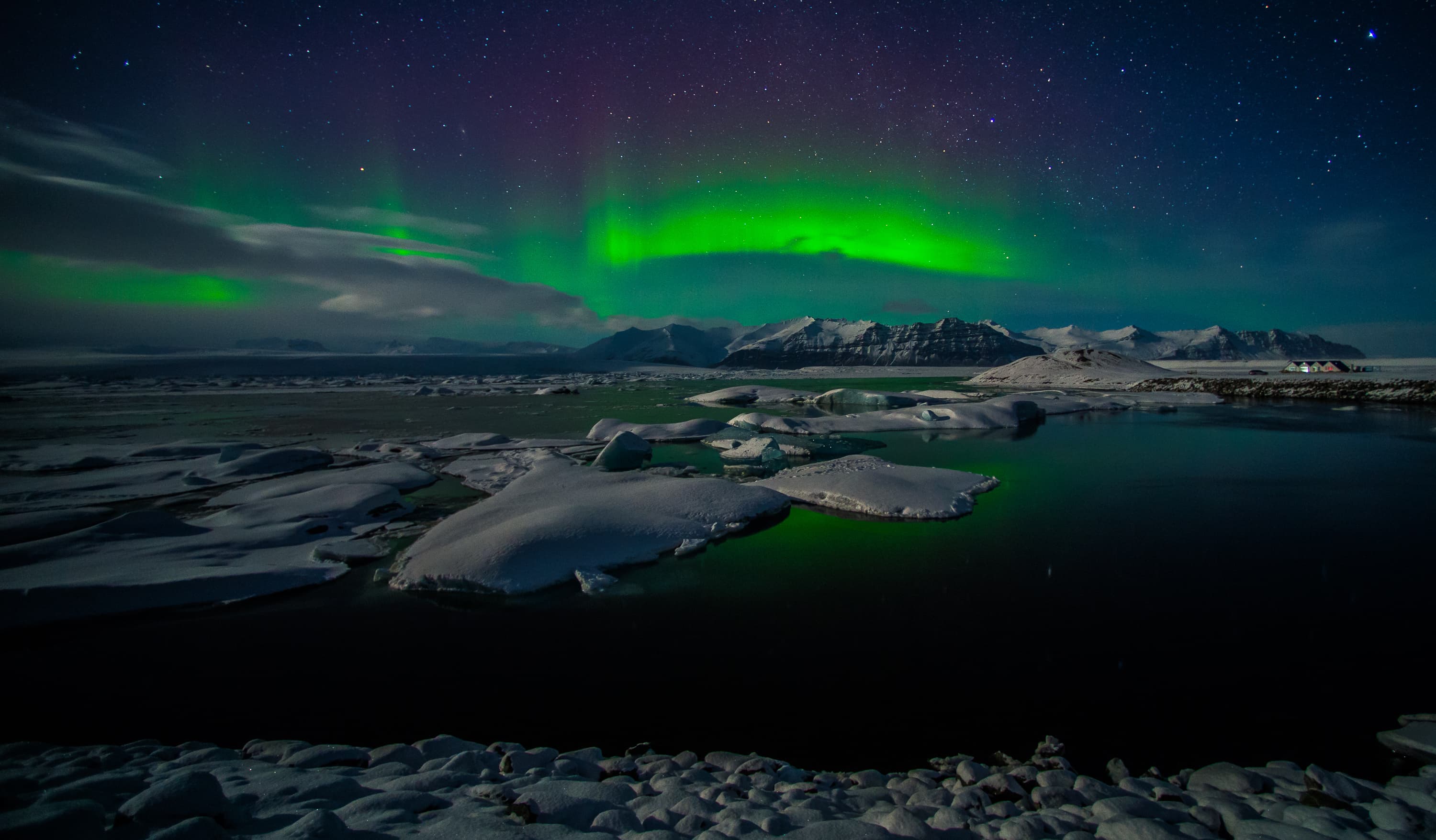 A beautiful green aurora borealis dancing over the Jokulsarlon lagoon, Iceland. In the forground is reflection in the lake surface. In the background are the northern lights above the mountains. A beautiful green aurora borealis dancing over the Jokulsarlon lagoon, Iceland. In the forground is reflection in the lake surface. In the background are the northern lights above the mountains.