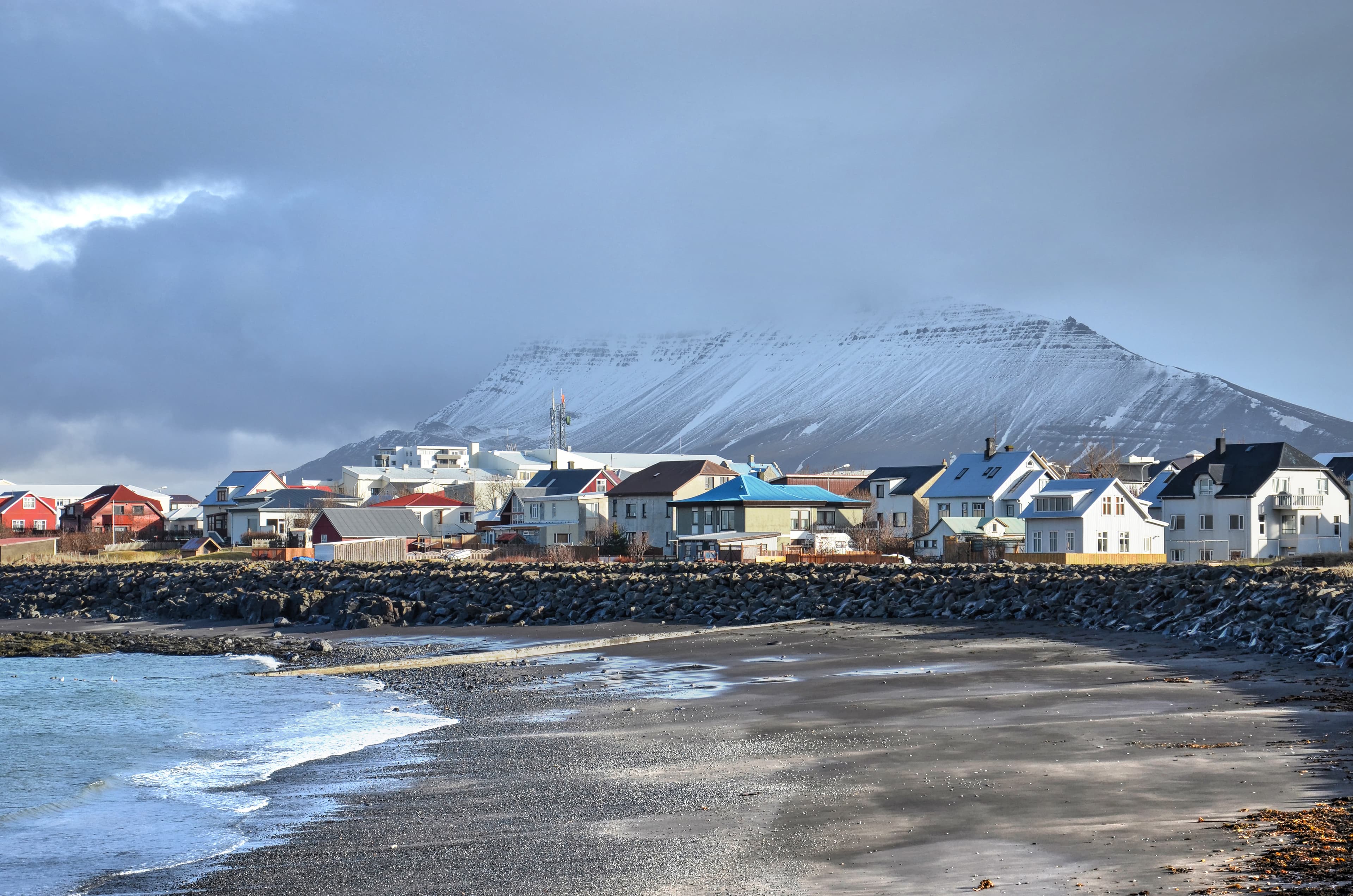 Akranes, Iceland, February 28, 2012: Colorful houses next to the beach with mountains partially obscured by clouds in the background The beach, the town and the mountains