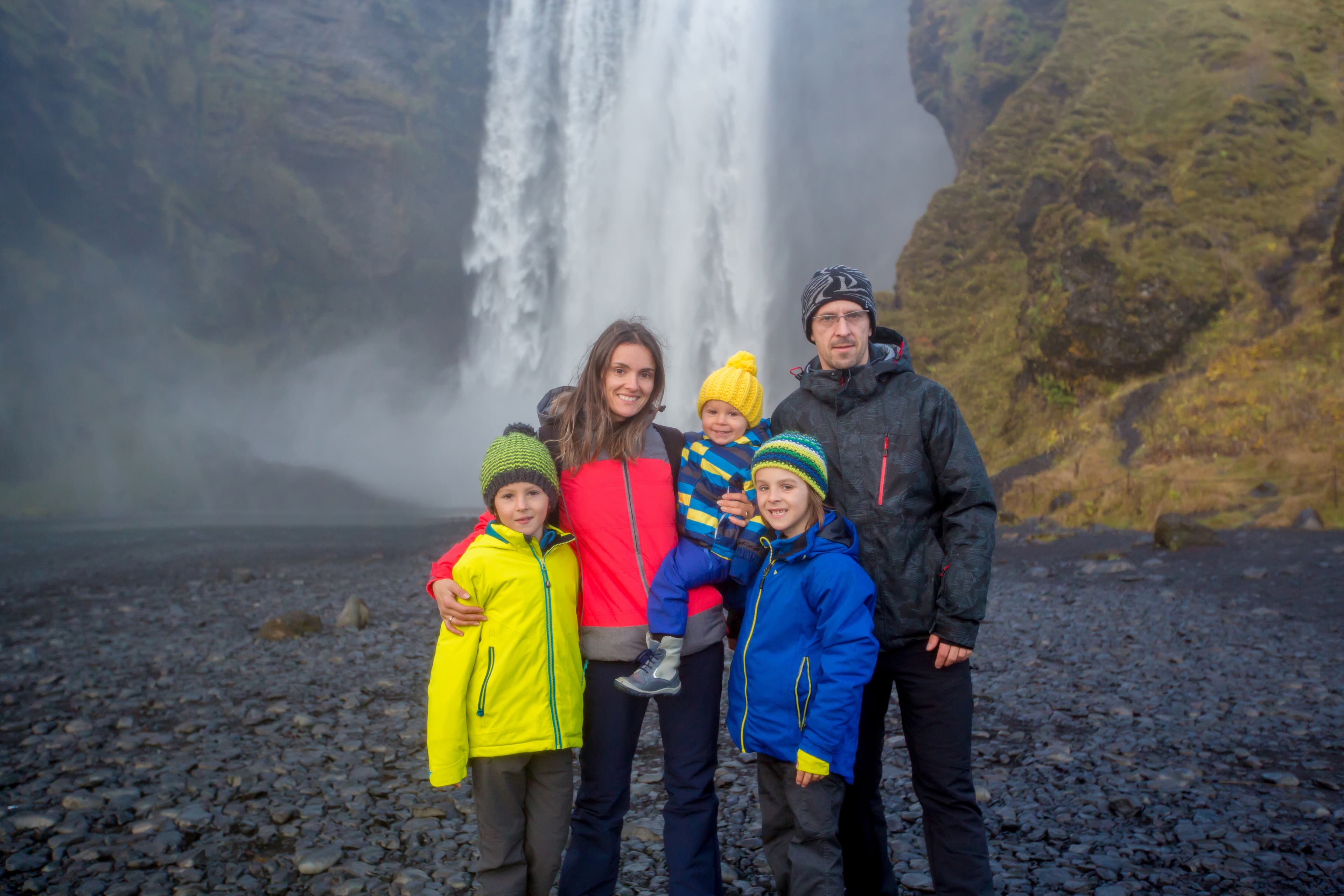 Happy family, posing in front of the Skogafoss waterfall in Iceland on a sunset cloudy day, autumntime Happy family, posing in front of the Skogafoss waterfall in Iceland on a sunset cloudy day
