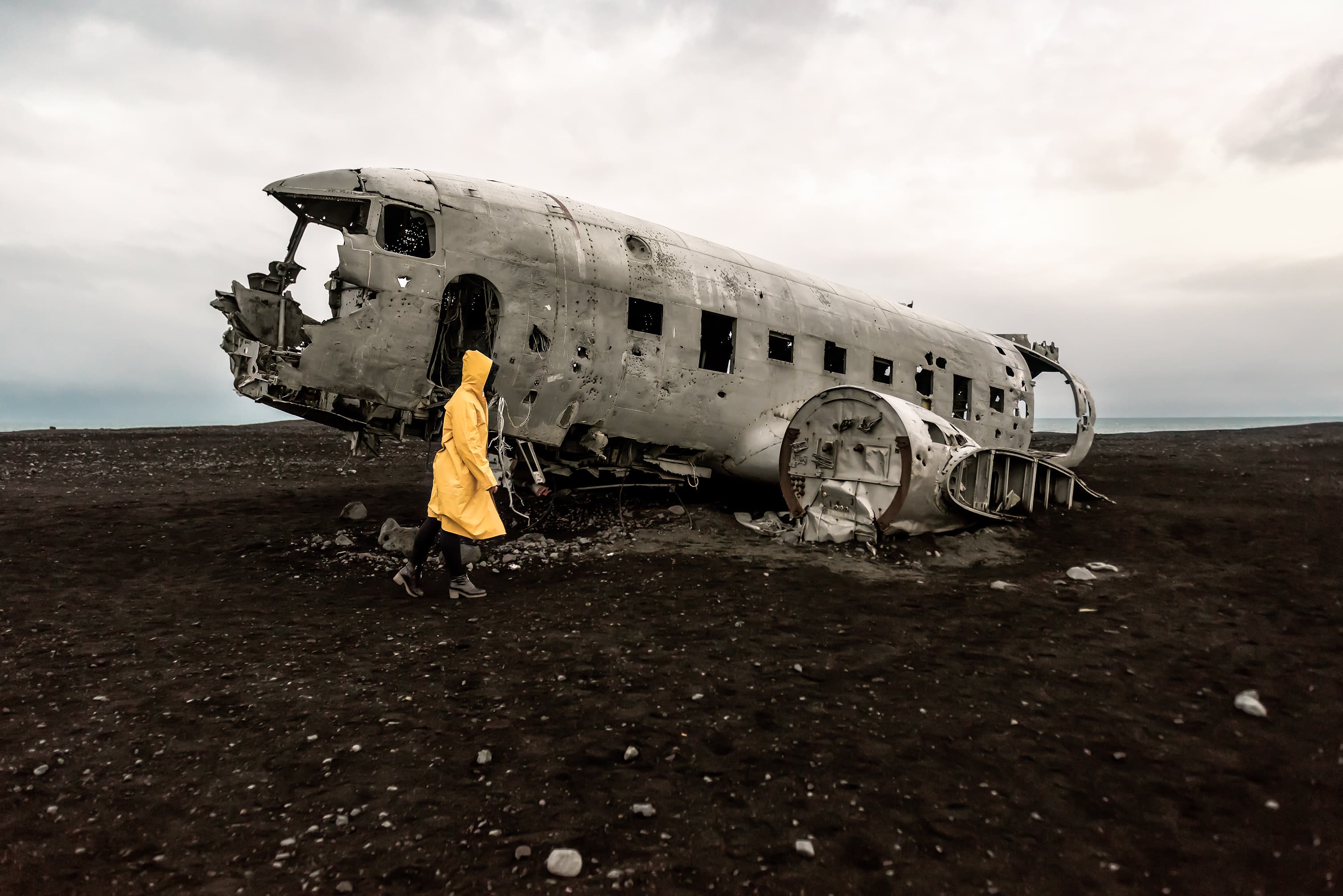 Girl in yellow raincoat near remains of the broken plane. Iceland girl in raincoat near remains of the broken plane