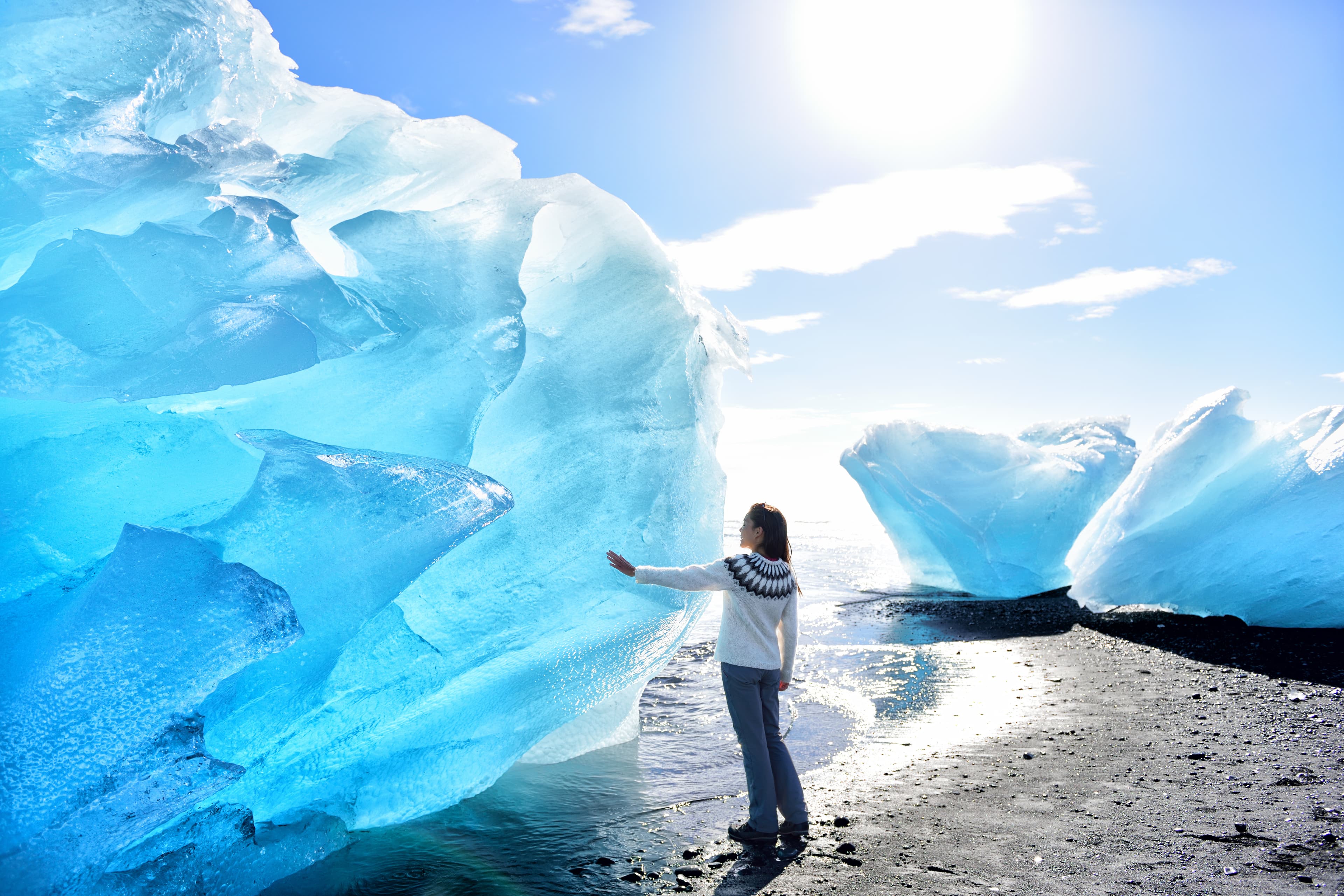 Iceland Amazing landscape at Iceberg beach. Tourist by icebergs on Ice beach, Breidamerkursandur aka Diamond Beach by jokulsarlon glacial lagoon / glacier lake nature. Woman in icelandic sweater. Iceland Amazing landscape at Iceberg beach. Tourist by icebergs on Ice beach, Breidamerkursandur aka Diamond Beach by jokulsarlon glacial lagoon / glacier lake nature. Woman in icelandic sweater