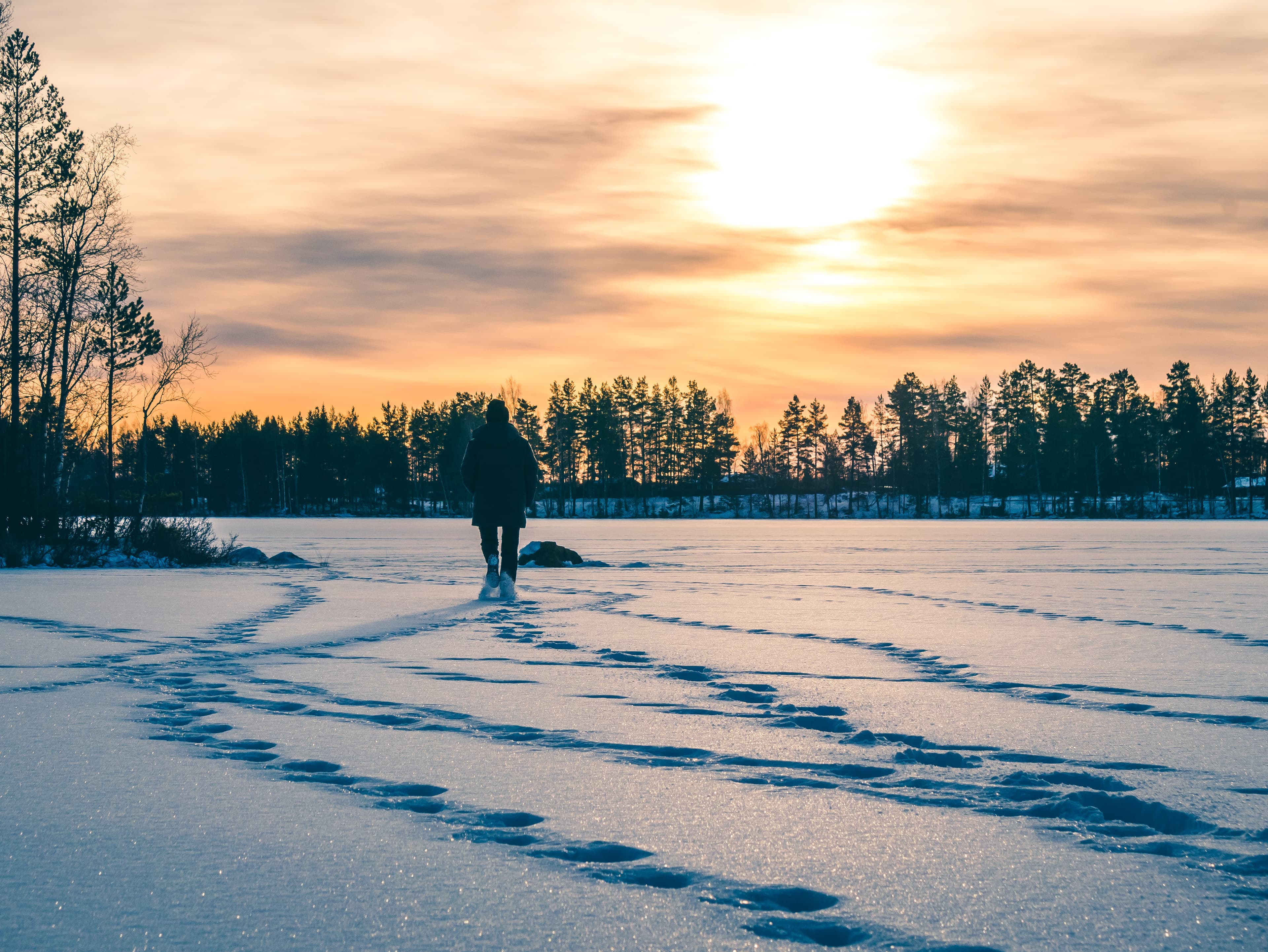 Person is walking on the snowy ice lake in sunset. Winter landscape. Person is walking on the snowy ice lake in sunset. Winter landscape.