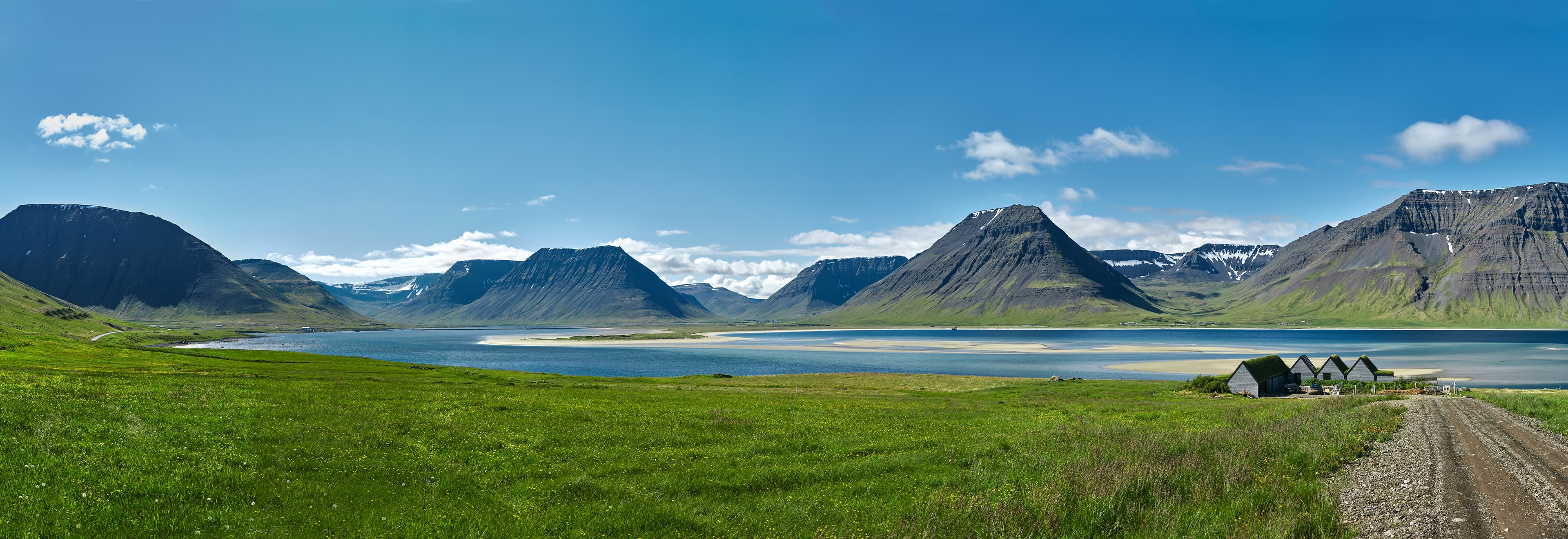 Travel to Iceland. beautiful sunrise over the ocean and fjord in Iceland. Icelandic landscape with mountains, blue sky and green grass on the foreground. View of the road to houses in the north-west of Iceland, on the Westfirdir peninsula beautiful sunrise over the fjord in Iceland