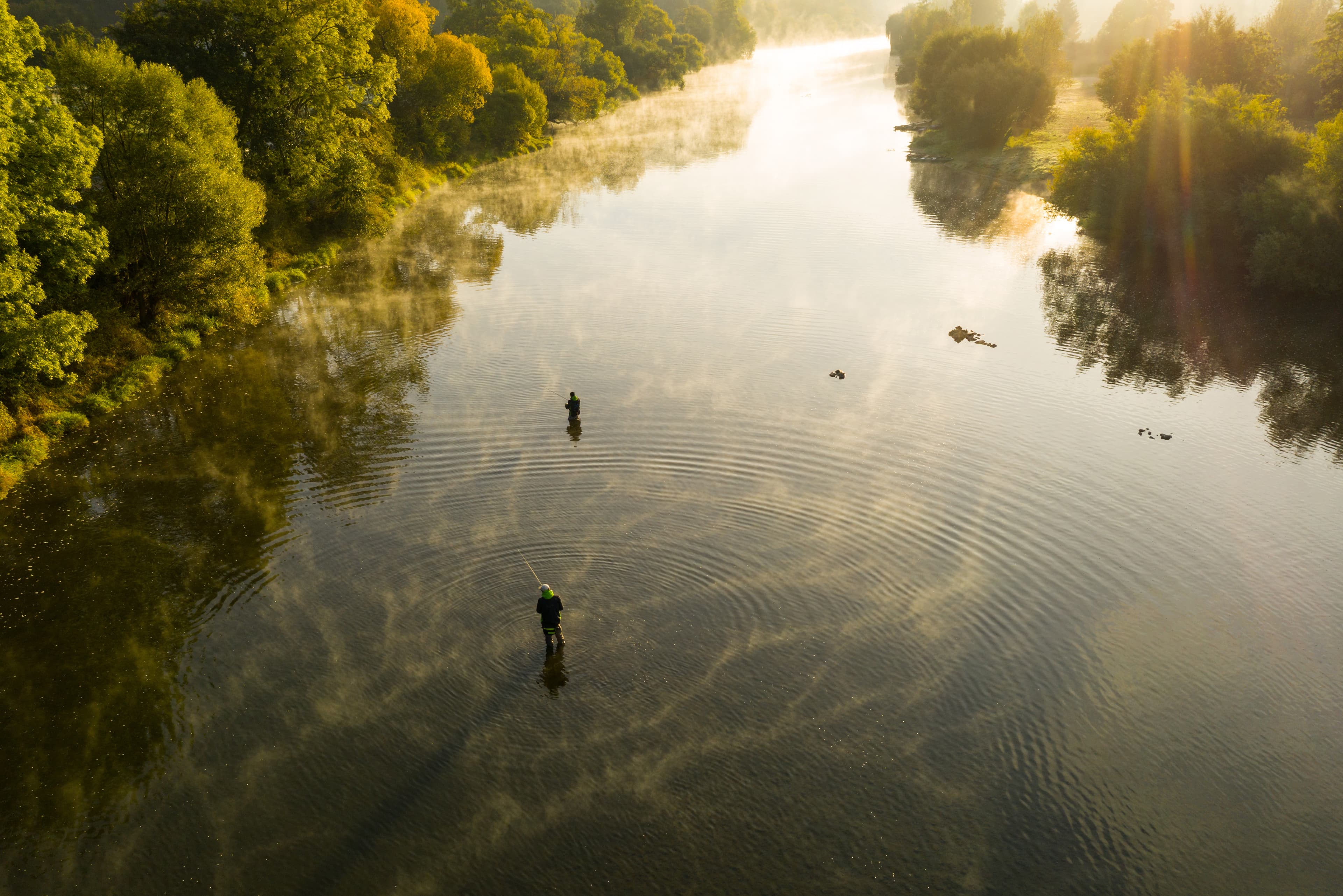 Aerial shot of a man fly fishing in a river with a fog during summer morning. Aerial shot of a man fly fishing in a river during summer morning.