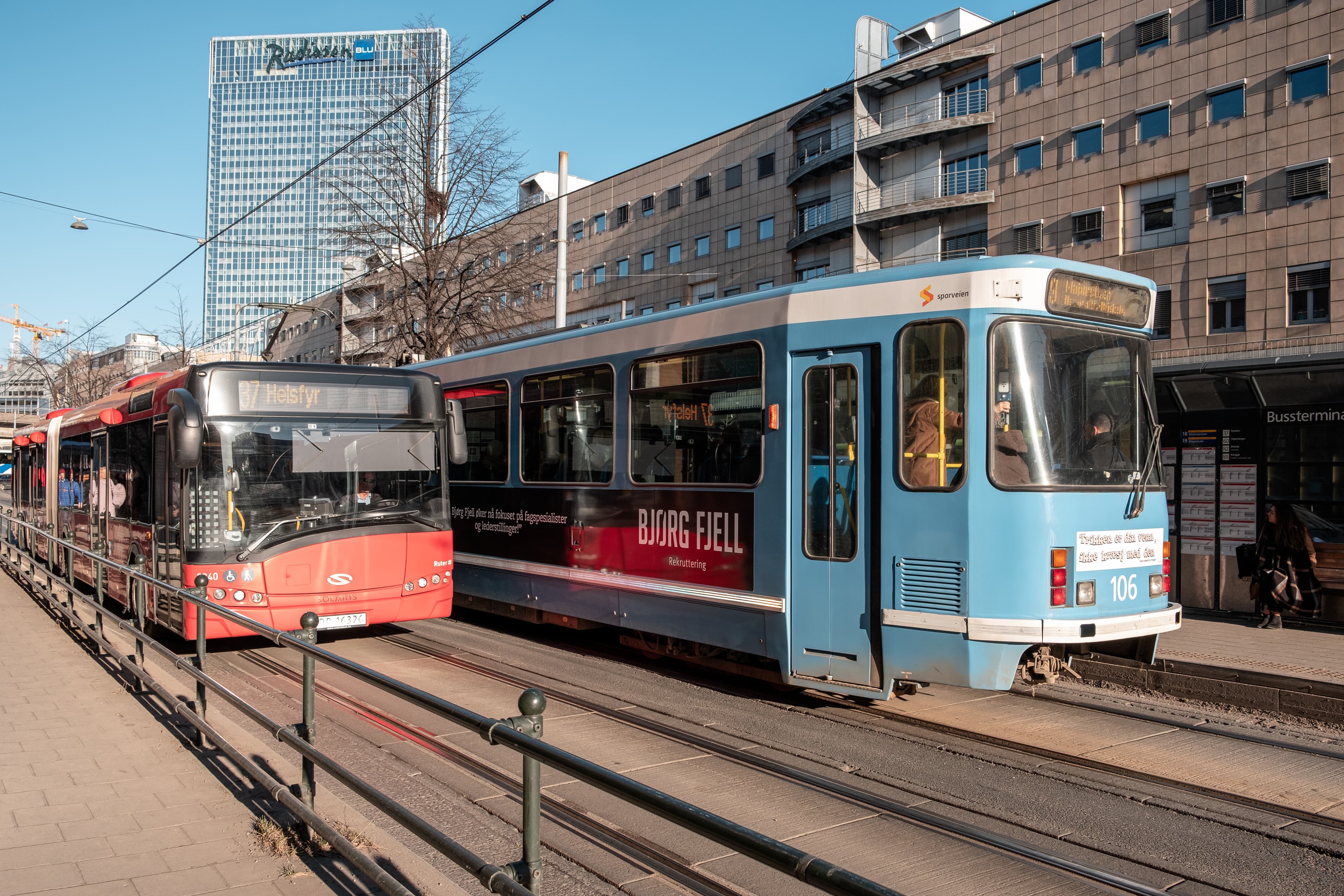 Oslo, Norway - Mar 27 2018 : Red and blue Tram with passenger running on electric rail with buildings in downtown Red and blue Tram with passenger running on electric rail with buildings in downtown