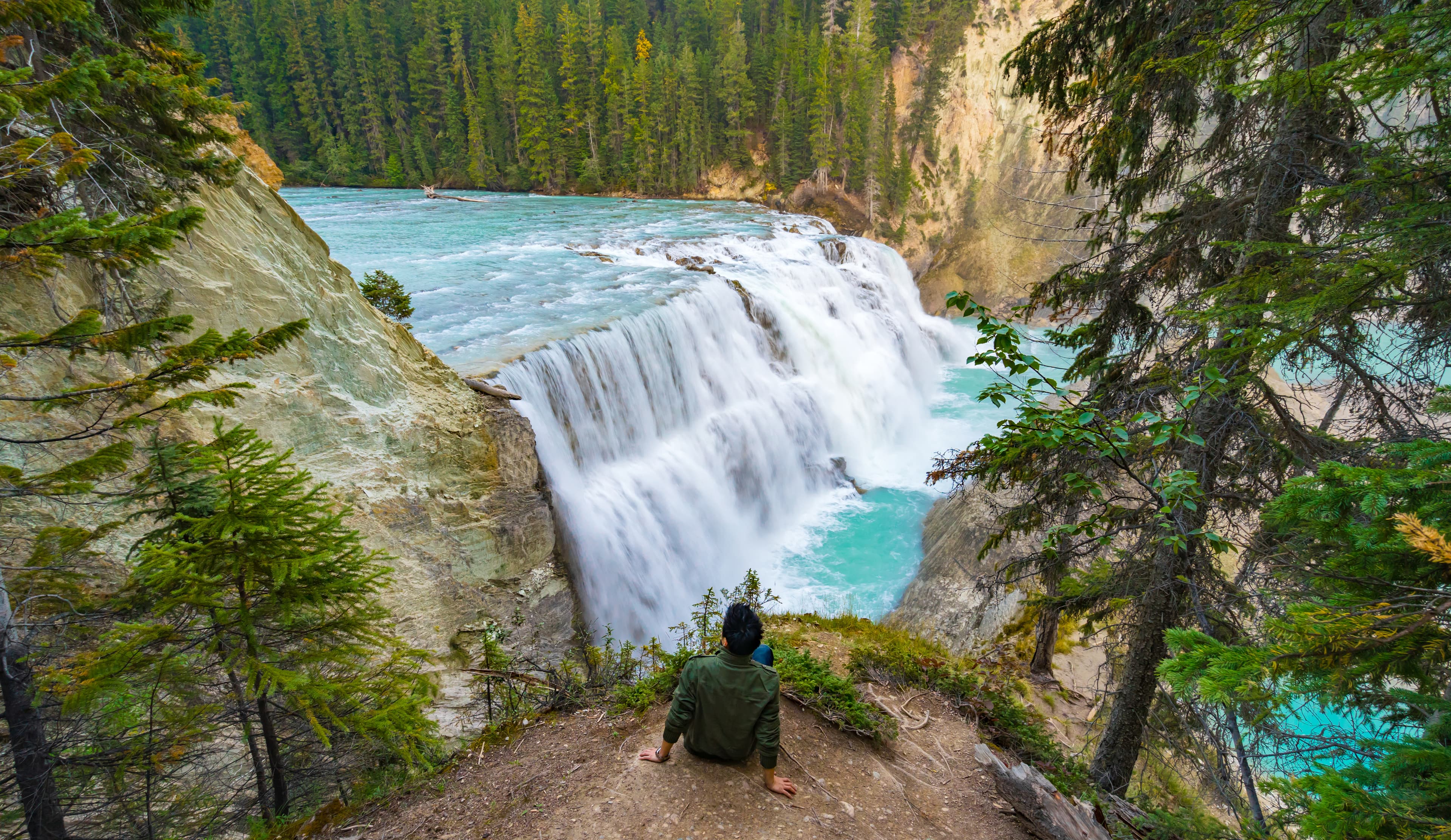 A man sitting on a ground looking at Wapta falls in Canada