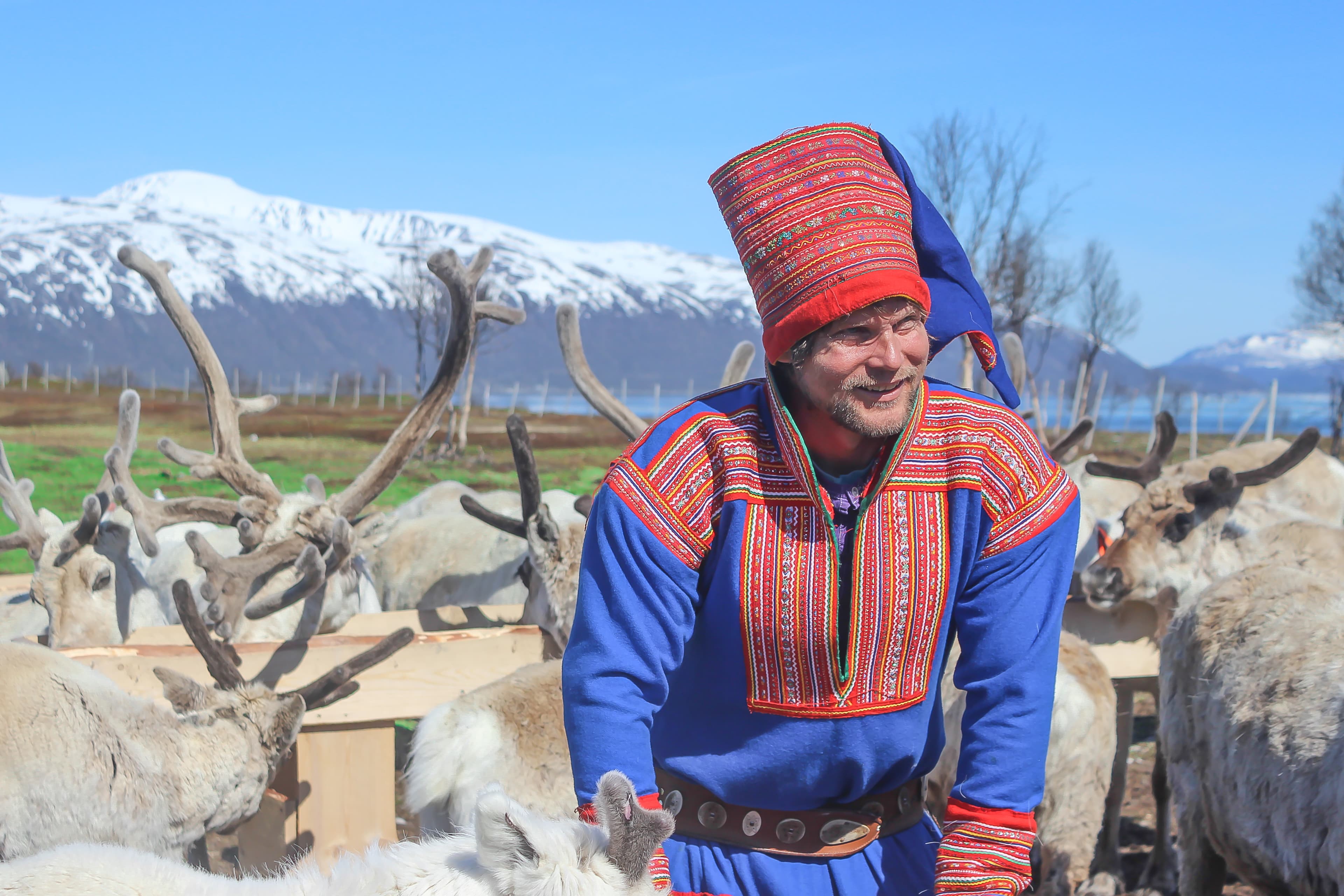happy-man-dressed-in-traditional-outfit-surrounded-by-reindeers