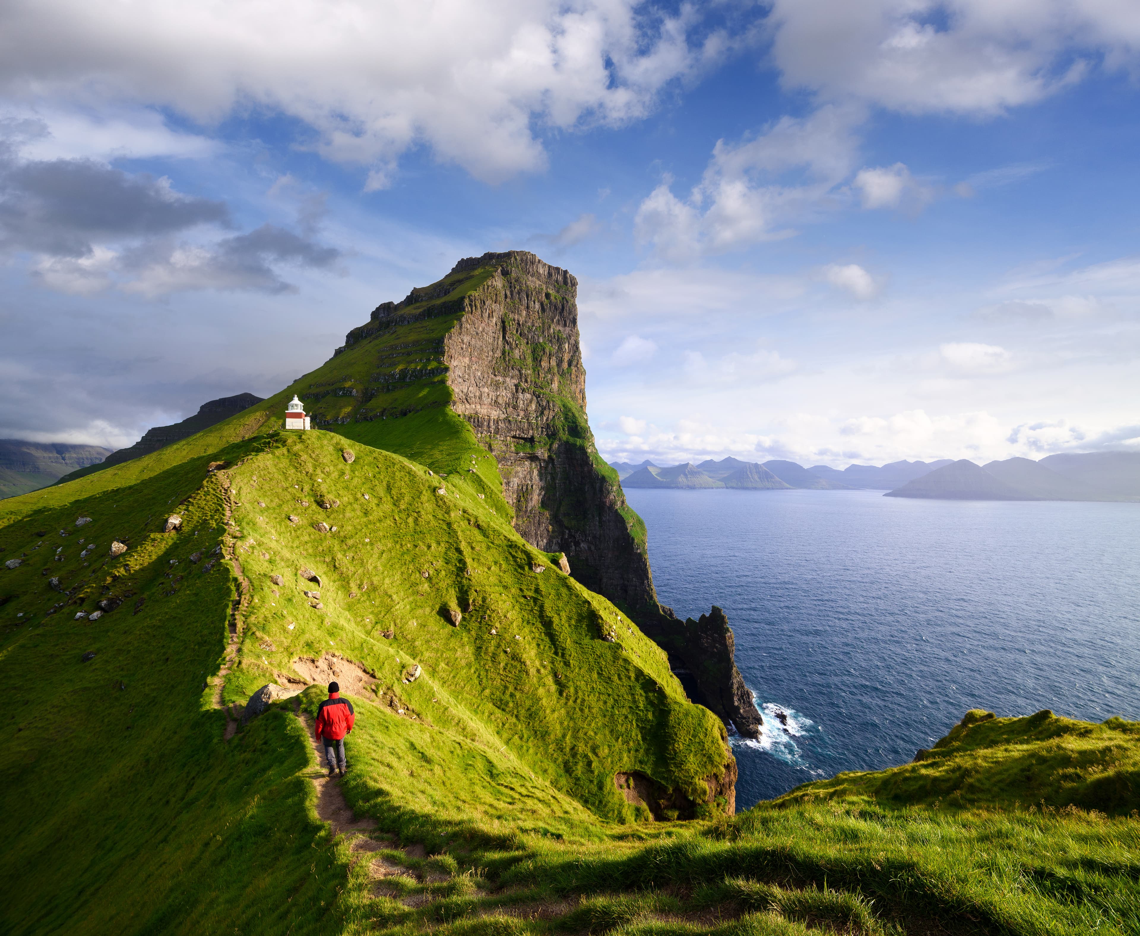 Kallur Lighthouse on Kalsoy island. Faroe islands, Kingdom of Denmark, Europe. Tourist in a red jacket visiting a tourist attraction. Summer mountain landscape Kallur Lighthouse on Kalsoy island, Faroe islands