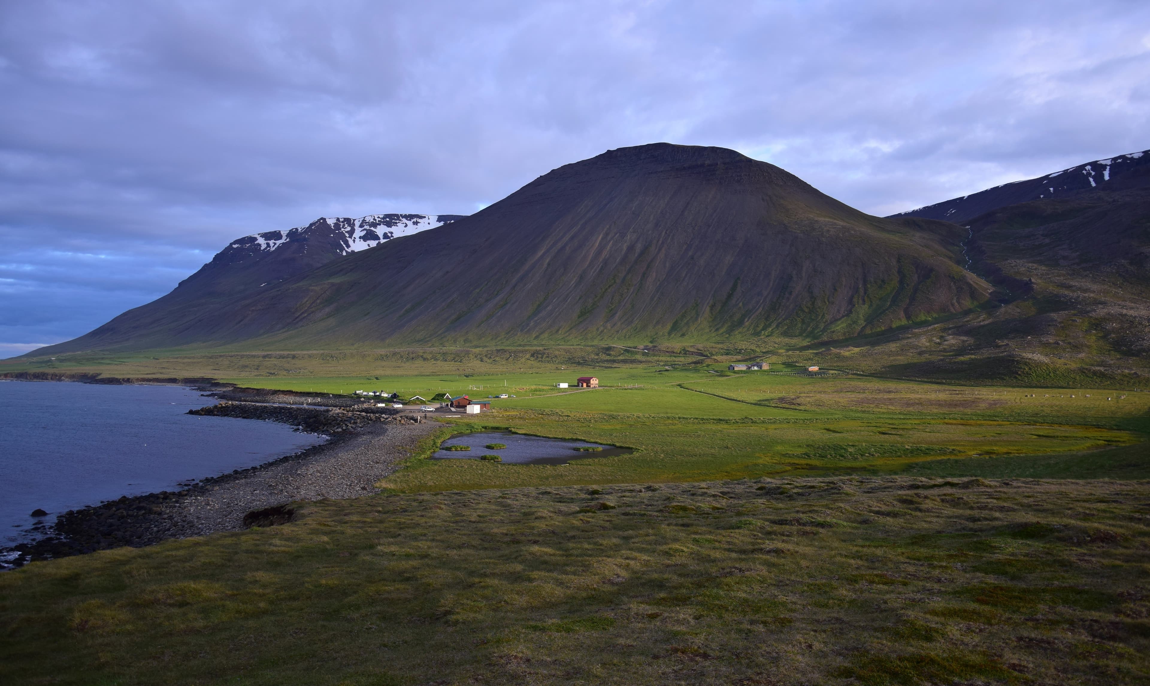 Icelandic landscape with the campsite at the hot pot Grettislaug on peninsula Skagi.A few buildings and in the background a mountain in the evening sun. Icelandic landscape with the campsite at the hot pot Grettislaug on peninsula Skagi.
