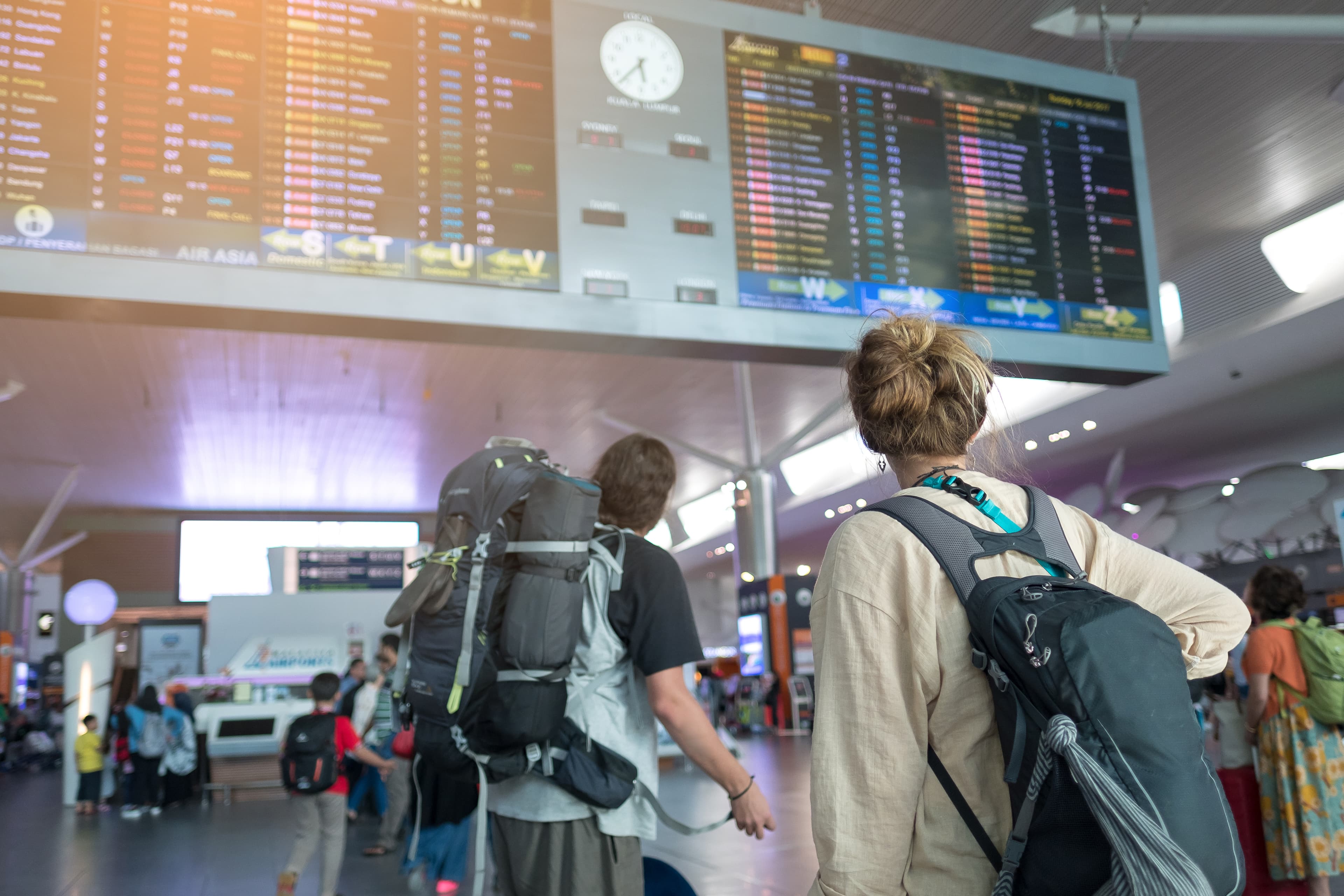 Young couple with backpack in airport near flight timetable Young couple with backpack in airport near flight timetable