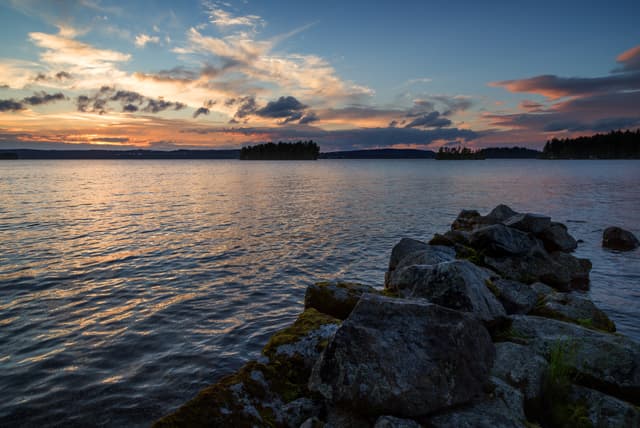 View of an old and broken pier made of rocks and lake at sunset in Finland in the summer.