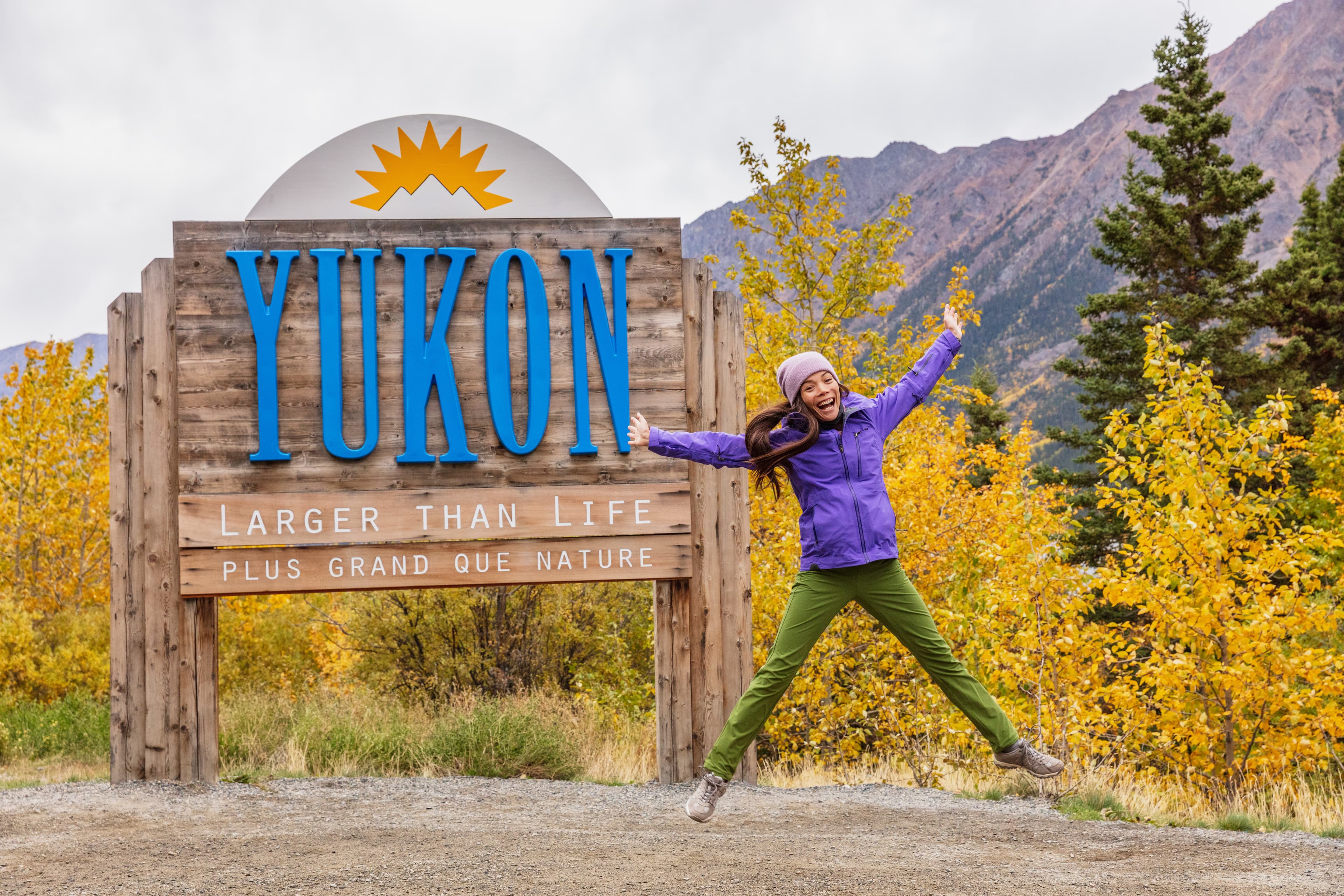 Yukon territory welcome sign - happy tourist woman jumping of fun in canadian territories. Alaska cruise travel autumn holiday. Yukon Territory Region 24