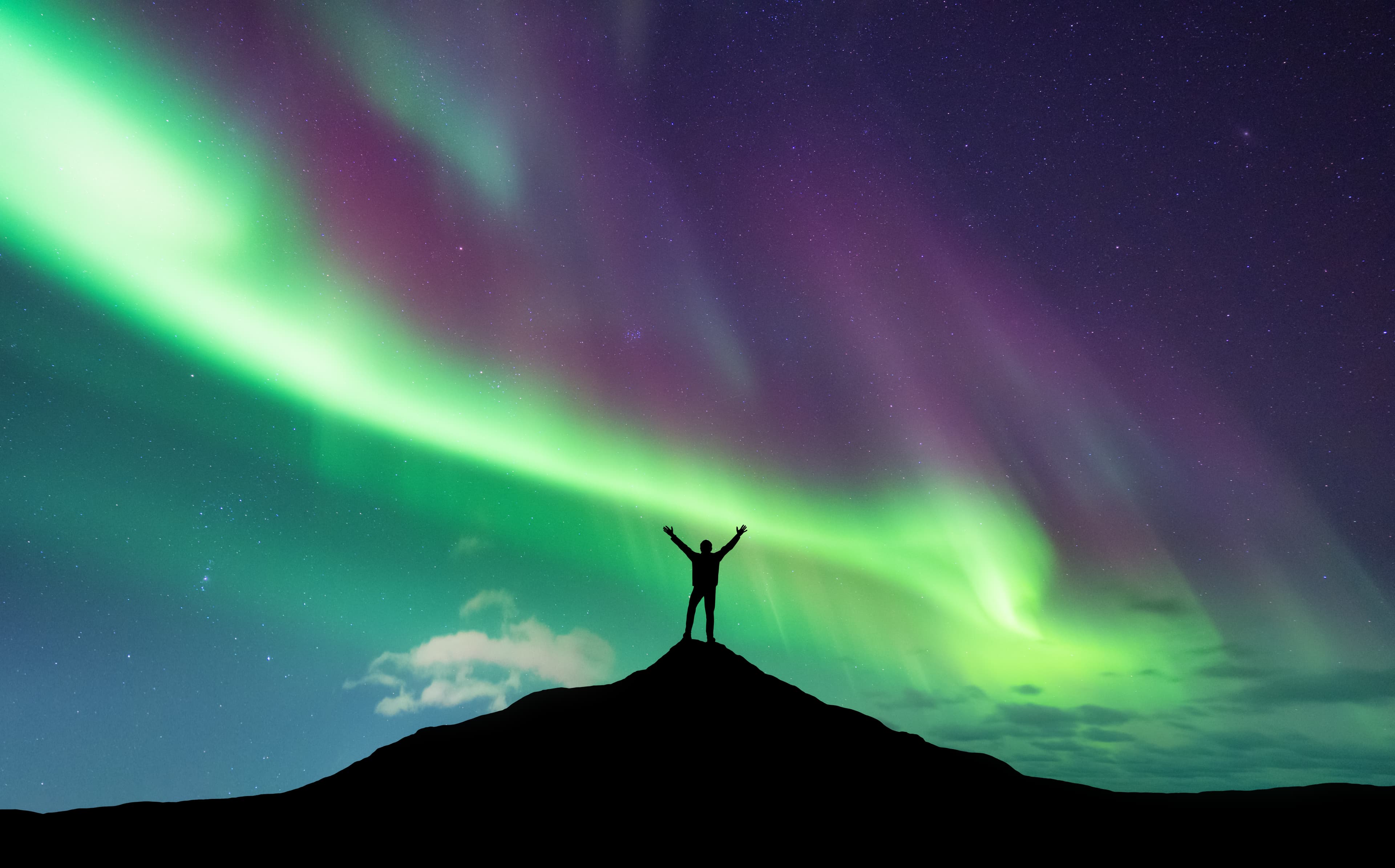 Northern lights and silhouette of standing man with raised up arms on the mountain peak in Norway. Aurora borealis and happy man. Sky with stars and polar lights. Night landscape with aurora. Concept northern-lights-silhouette-man-iceland
