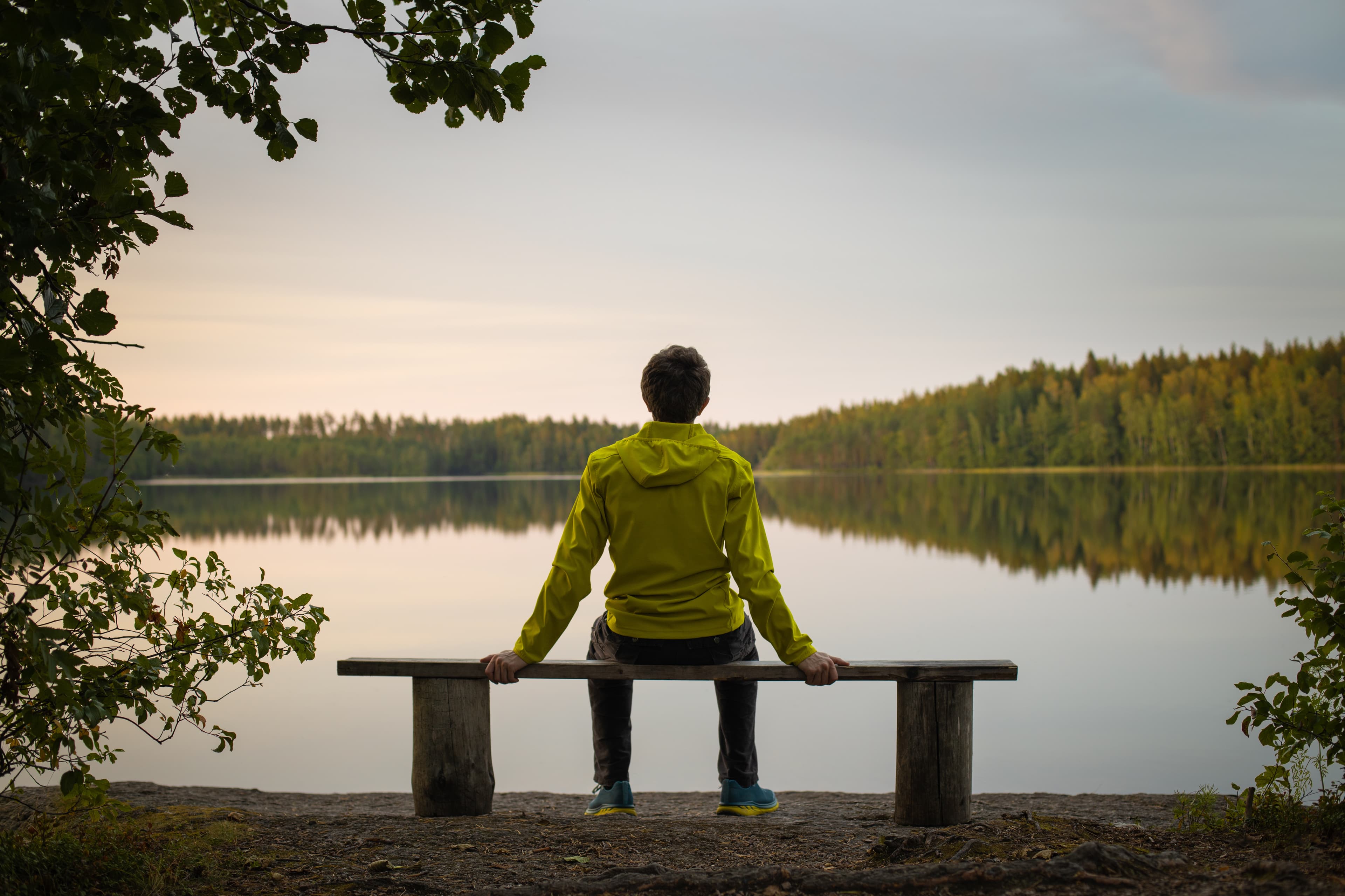 A man in a yellow jacket sits on a bench by the lake on an autumn evening. Blurred background A man in a yellow jacket sits on a bench by the lake on an autumn evening. Blurred background