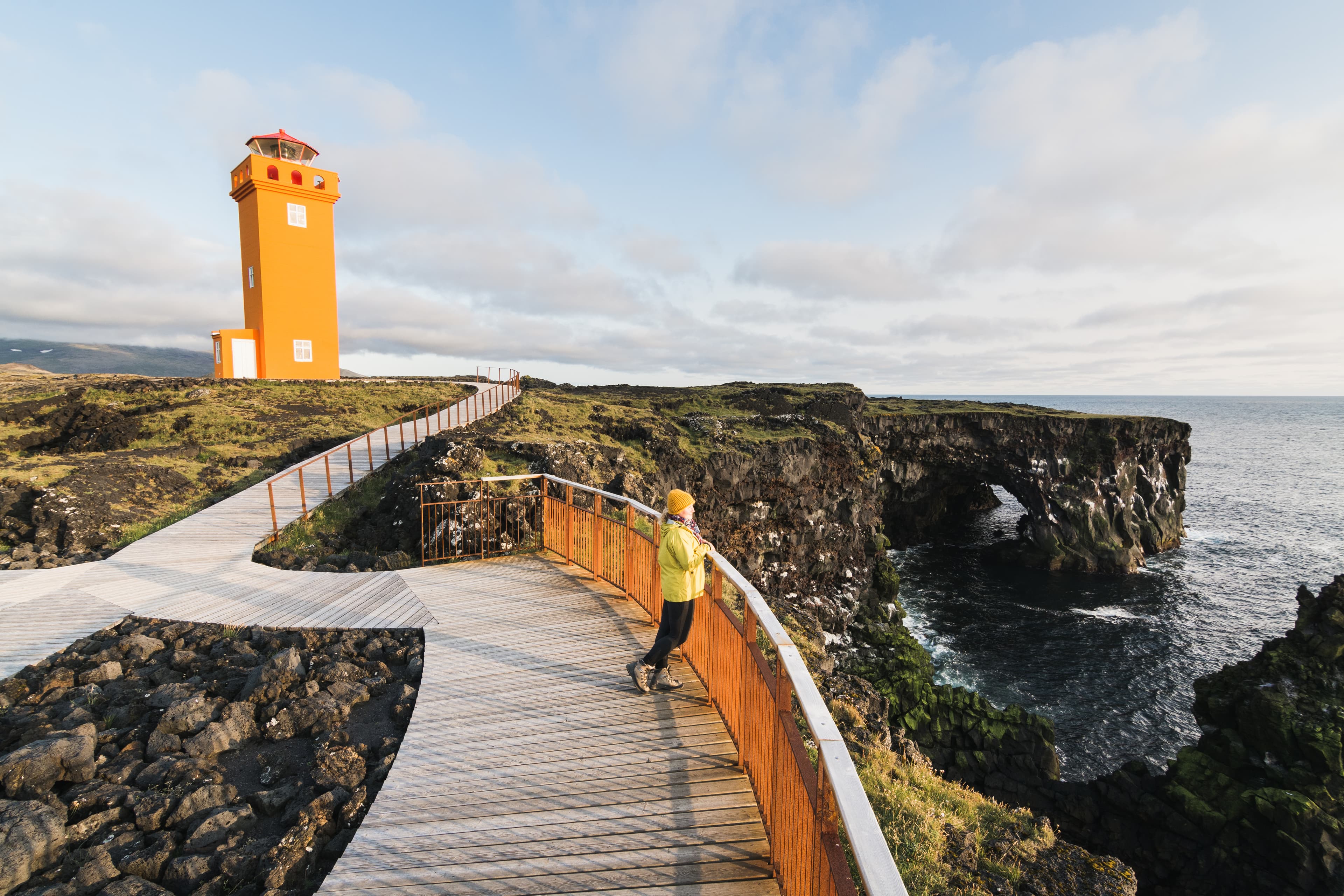 SNAEFELLSNES, ICELAND - AUGUST 2018: woman in yellow raincoat watching sunset at Svortuloft Lighthouse. SNAEFELLSNES, ICELAND - AUGUST 2018: woman in yellow raincoat watching sunset at Svortuloft Lighthouse