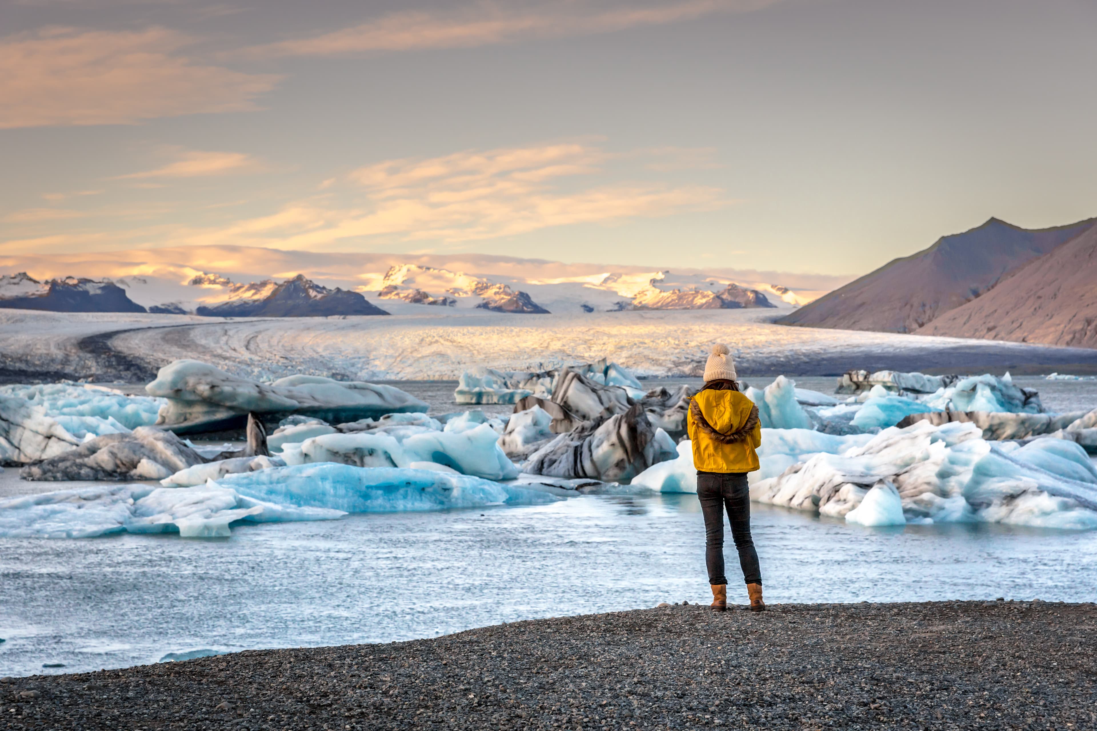 Young woman dressing cold clothes seeing the amazing Jokulsarlon, iceberg lagoon in Iceland Woman-near-Jokulsarlon-glacier-lagoon