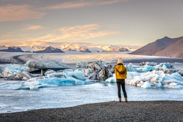 Young woman dressing cold clothes seeing the amazing Jokulsarlon, iceberg lagoon in Iceland Woman-near-Jokulsarlon-glacier-lagoon