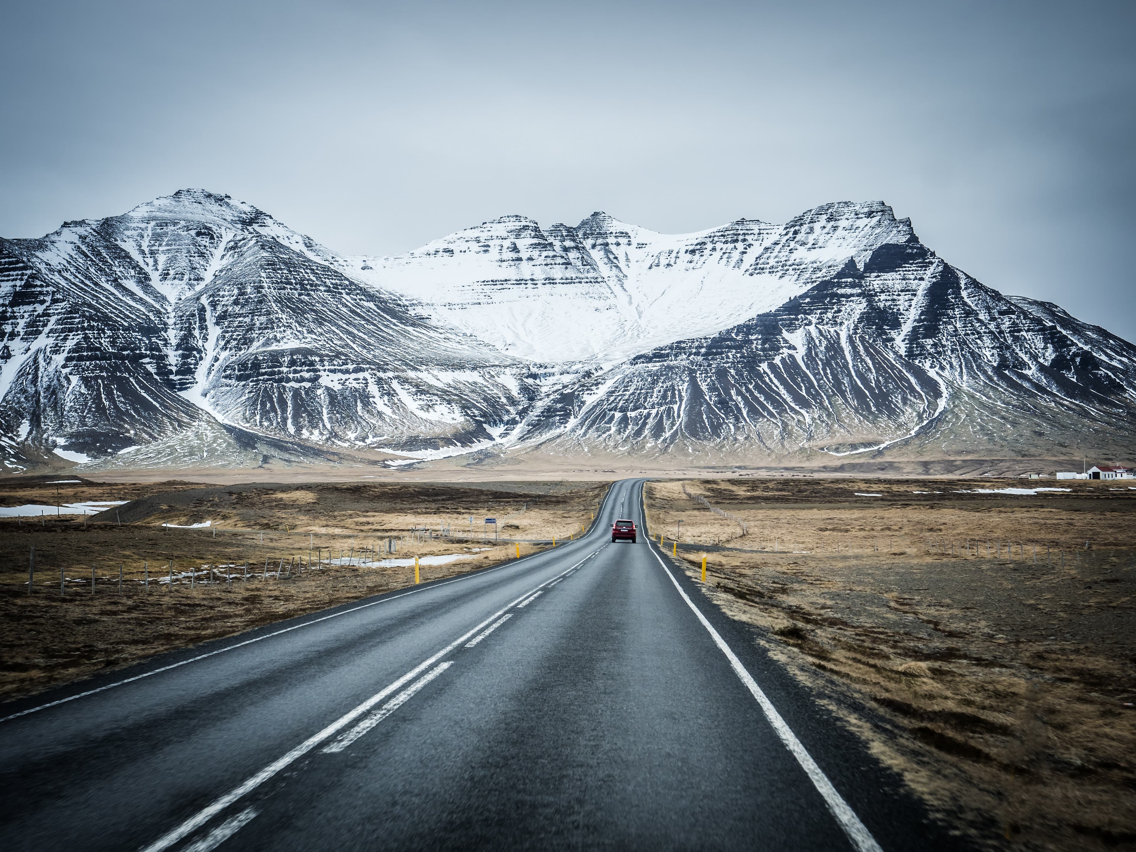 Modern car riding on asphalt countryside road towards magnificent snowy mountains during trip through Iceland Car riding towards mountains in Iceland in winter
