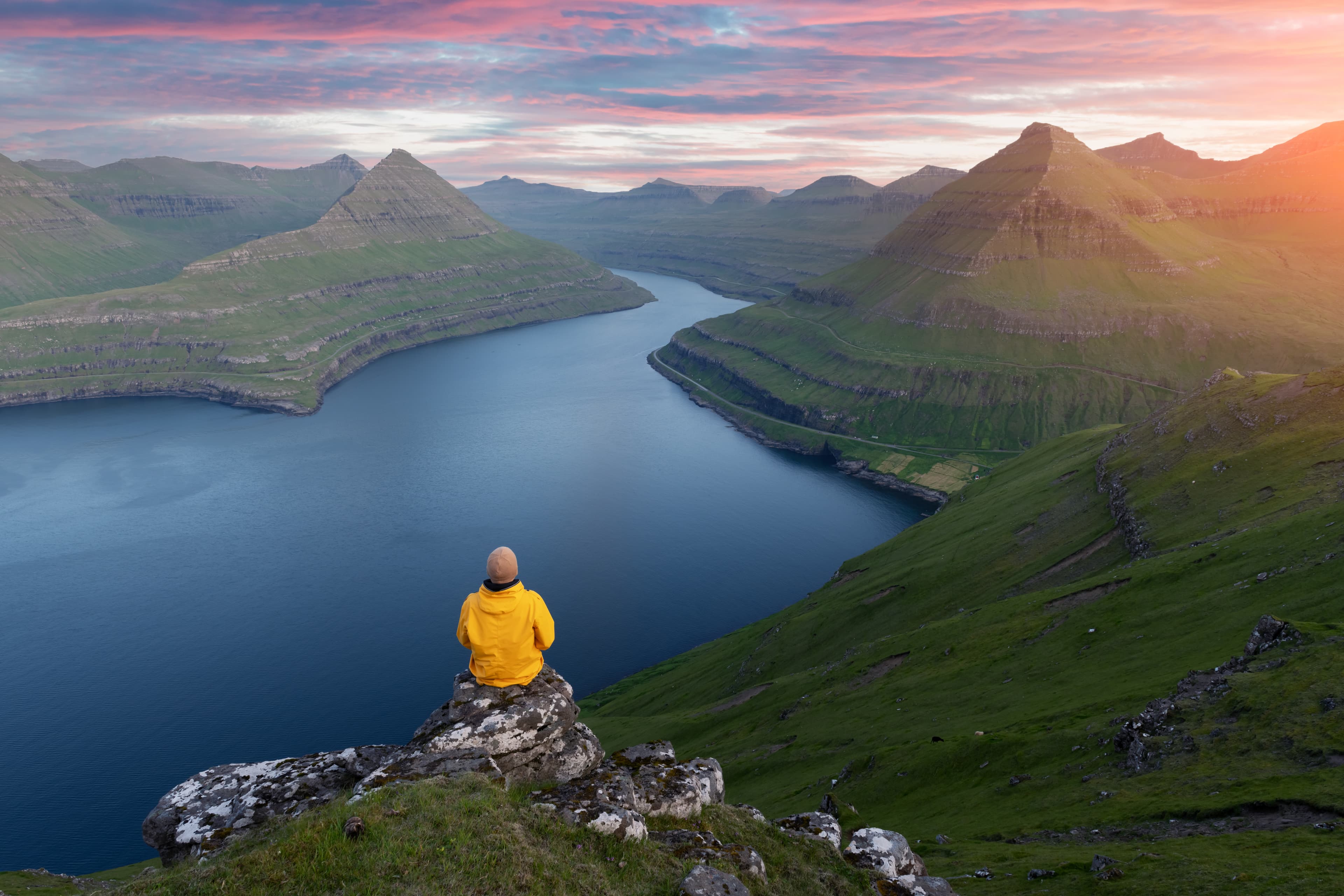 Lonely tourist in yellow jacket looking over majestic fjords of Funningur, Eysturoy island, Faroe Islands. Landscape photography Majestic views over the fjords of Funningur