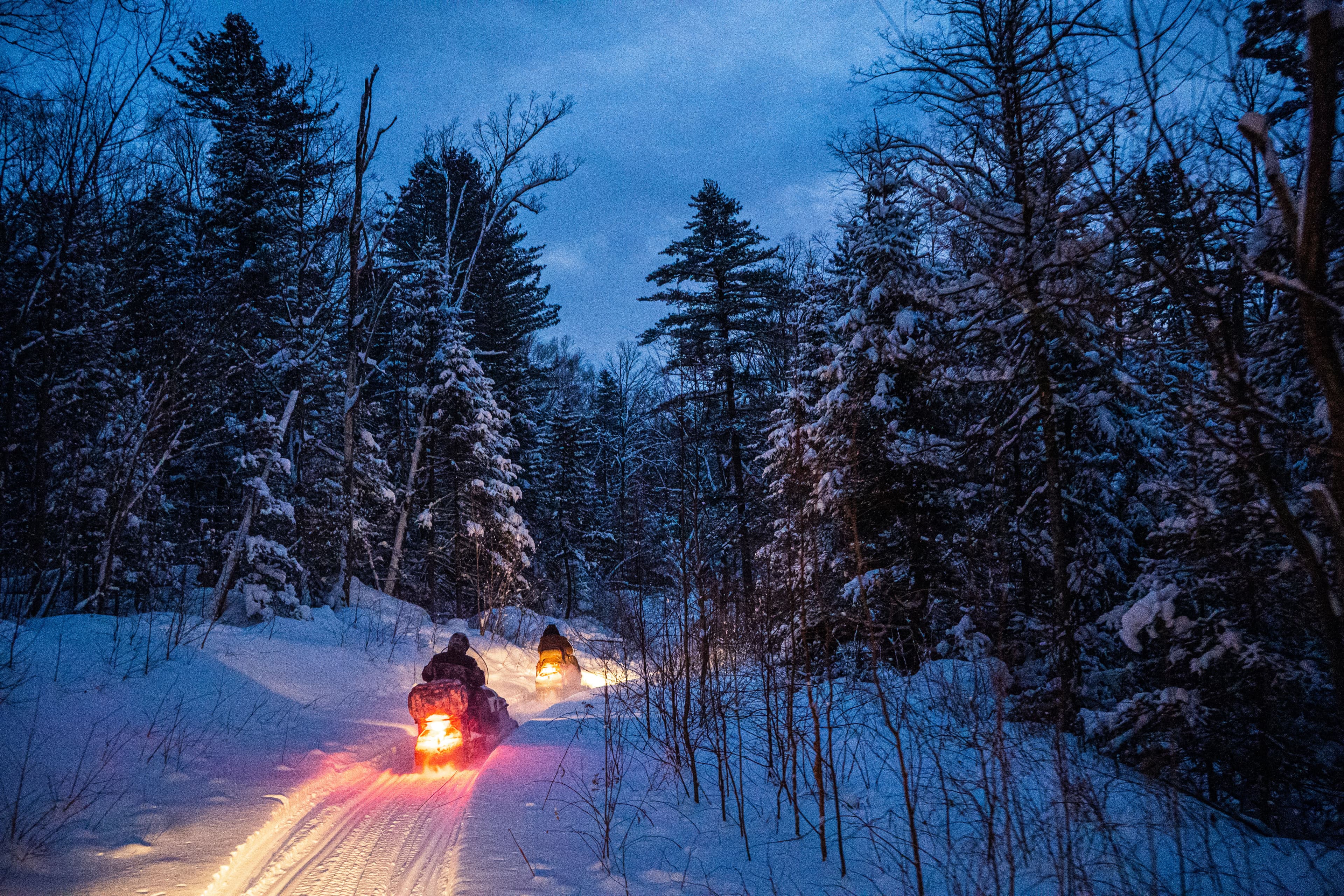 snowmobile in the evening goes through the winter forest. headlights. night road through the winter forest. snowmobile at night. snowmobile in the evening goes through the winter forest. headlights. night road through the winter forest. snowmobile at night