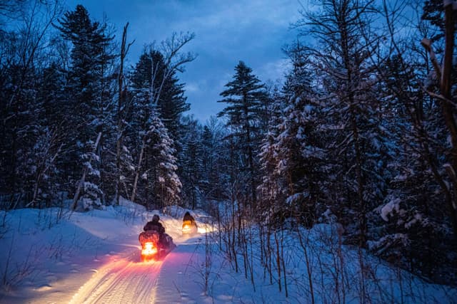 snowmobile in the evening goes through the winter forest. headlights. night road through the winter forest. snowmobile at night. snowmobile in the evening goes through the winter forest. headlights. night road through the winter forest. snowmobile at night