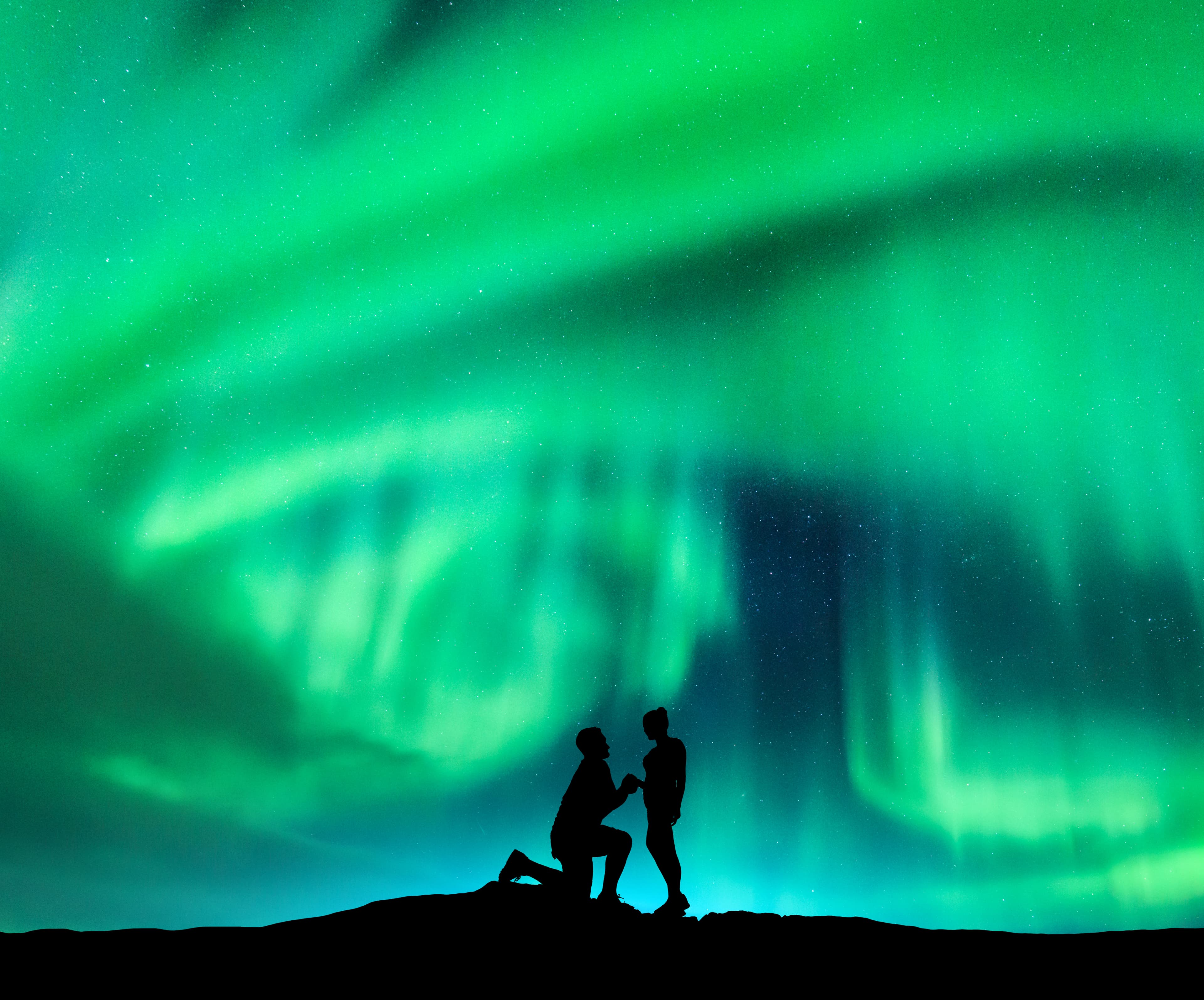 Aurora borealis and silhouette of a man making marriage proposal to his girlfriend. Night landscape with northern lights, starry sky and lovers. Couple, relationship. Aurora with people. Polar lights Aurora borealis and silhouette of a man making marriage proposal to his girlfriend. Night landscape with northern lights, starry sky and lovers. Couple, relationship. Aurora with people. Polar lights