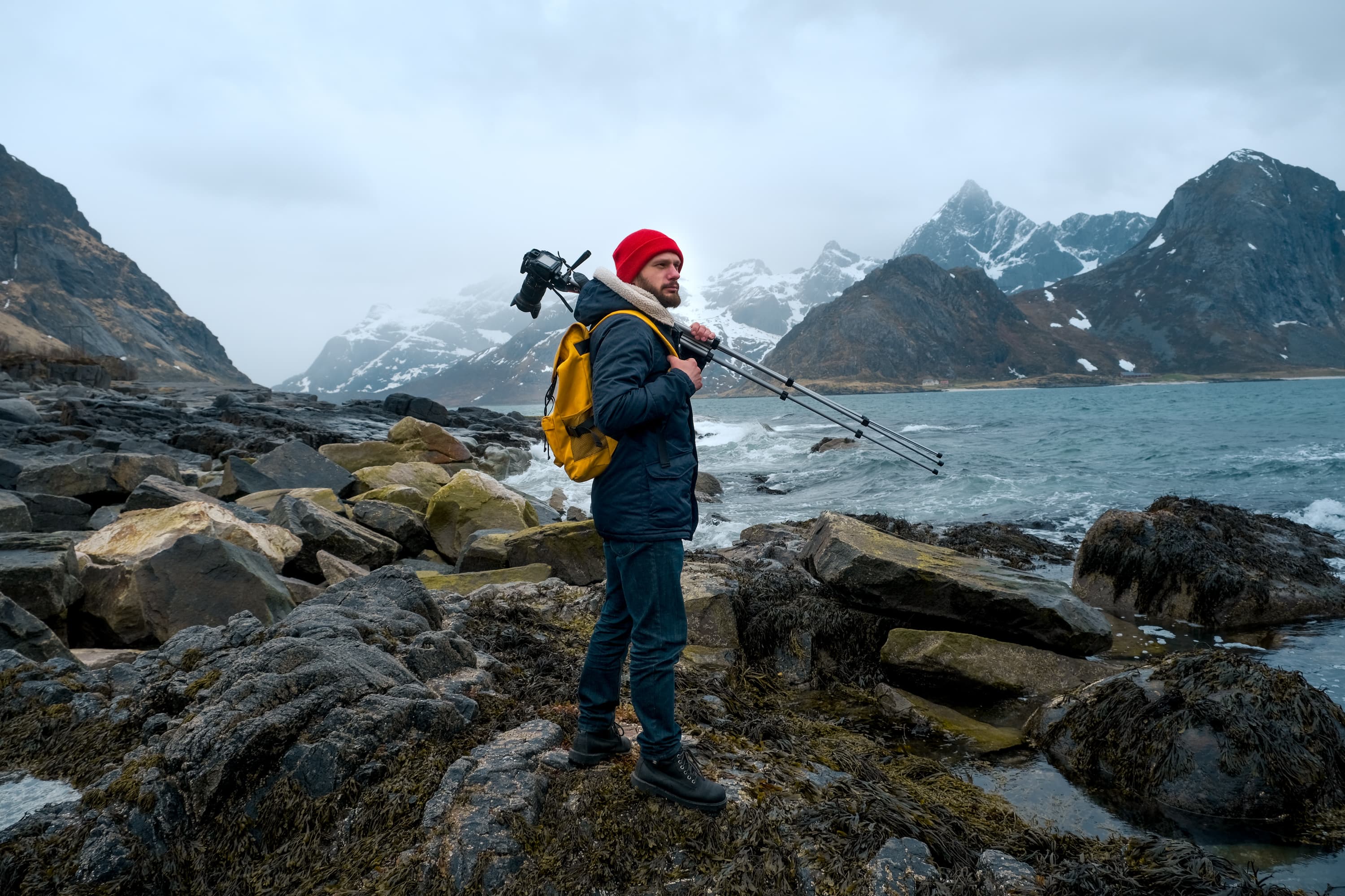 Young man photographer standing at rock in the mountains at Bunes Beach photographing the landscapes on Lofoten Islands in Norway Young man photographer standing at rock in the mountains at Beach photographing the landscapes on Lofoten Islands in Norway.