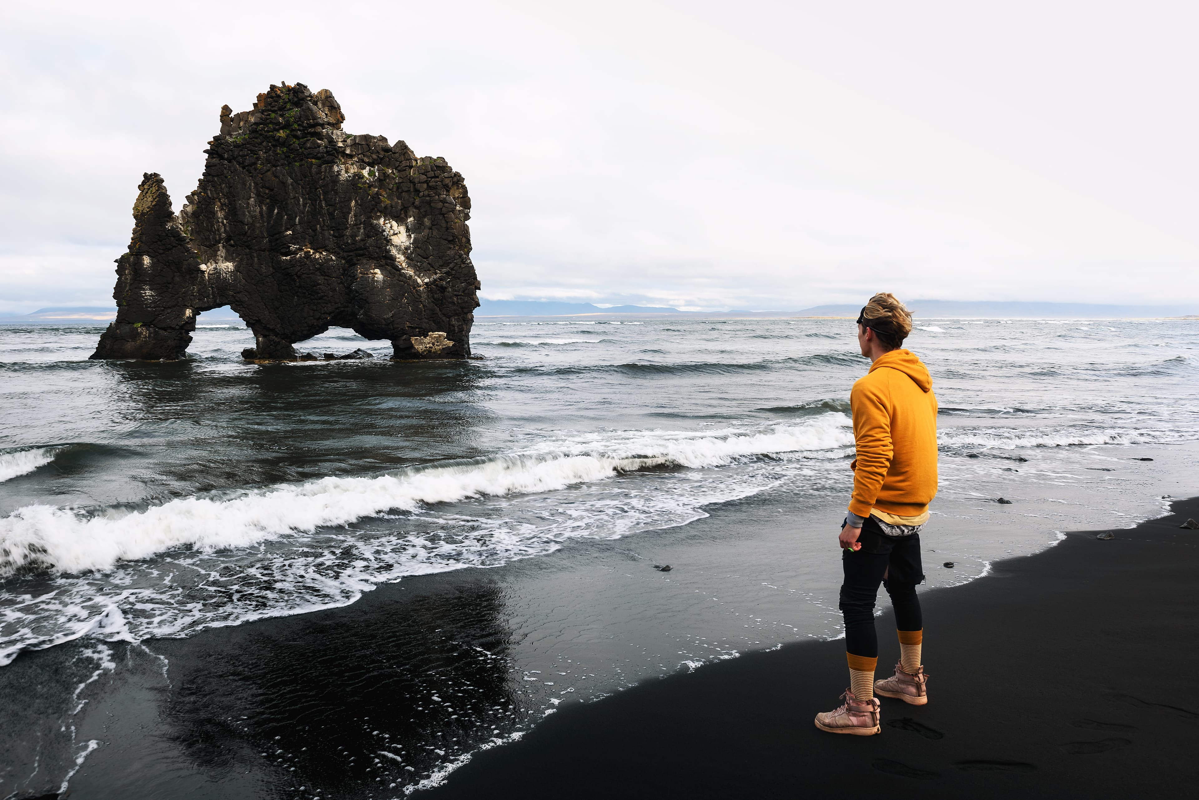 Tourist looks at the Hvitserkur basalt stack in northern Iceland. Hvitserkur is a spectacular rock in a shape of a dragon or dinosaur drinking water from the ocean. Tourist looks at the Hvitserkur basalt stack in northern Iceland