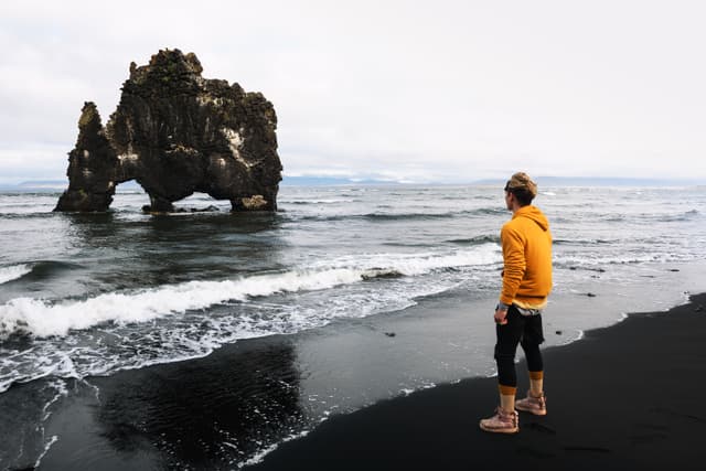 Tourist looks at the Hvitserkur basalt stack in northern Iceland. Hvitserkur is a spectacular rock in a shape of a dragon or dinosaur drinking water from the ocean. Tourist looks at the Hvitserkur basalt stack in northern Iceland