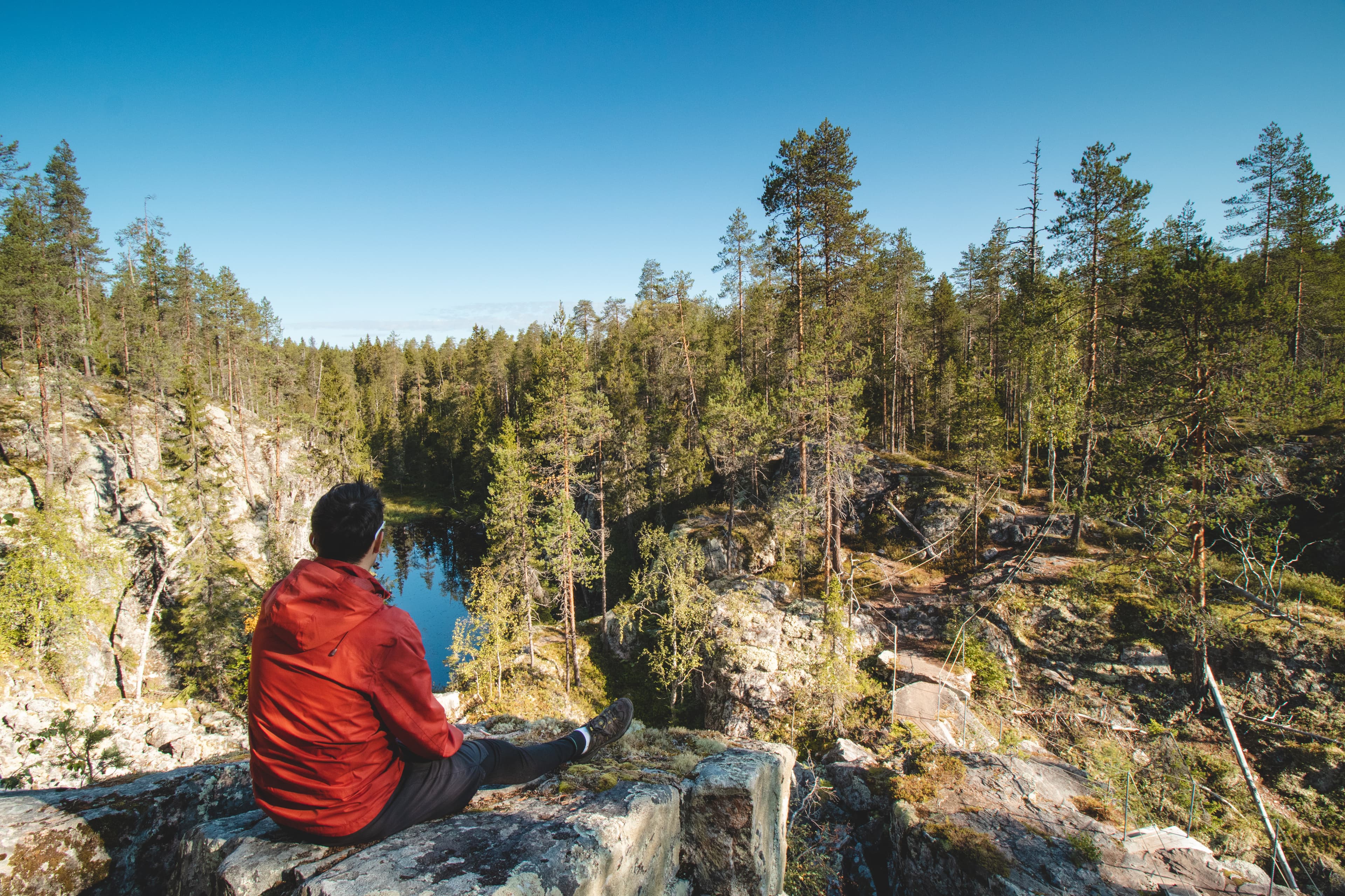 traveller sits on a high rock and observes a beautiful natural lake in hiidenportti national park, Sotkamo in kainuu region, Finland. Hiking the Finnish countryside. traveller sits on a high rock and observes a beautiful natural lake in hiidenportti national park, Sotkamo in kainuu region, Finland. Hiking the Finnish countryside