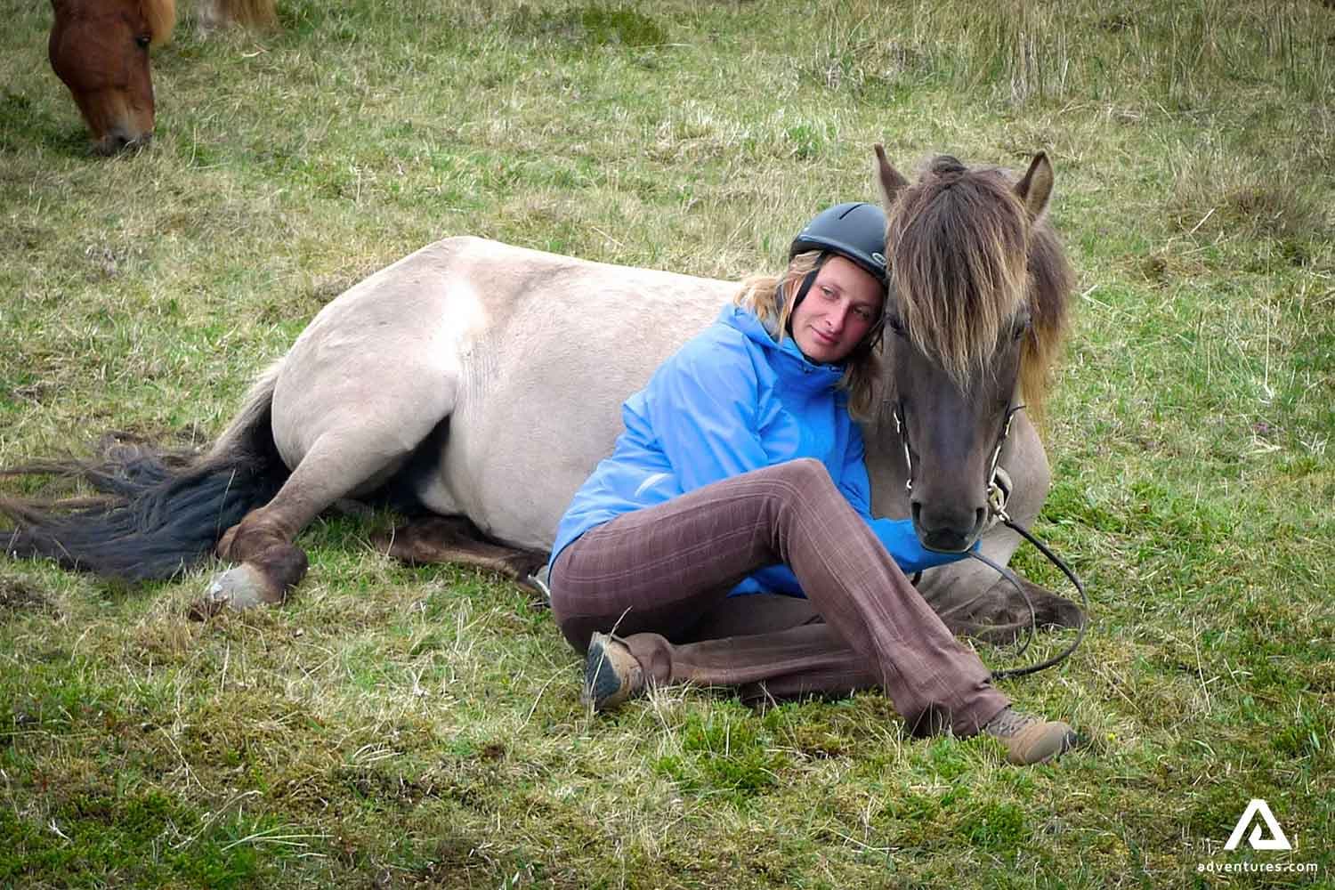 a-woman-lying-by-a-horse-on-a-grass-field-in-iceland