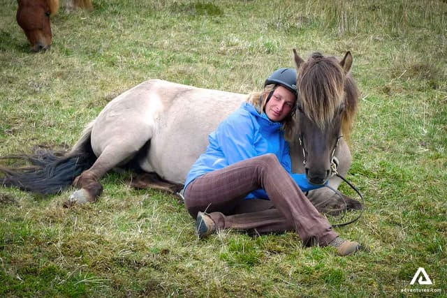 a-woman-lying-by-a-horse-on-a-grass-field-in-iceland