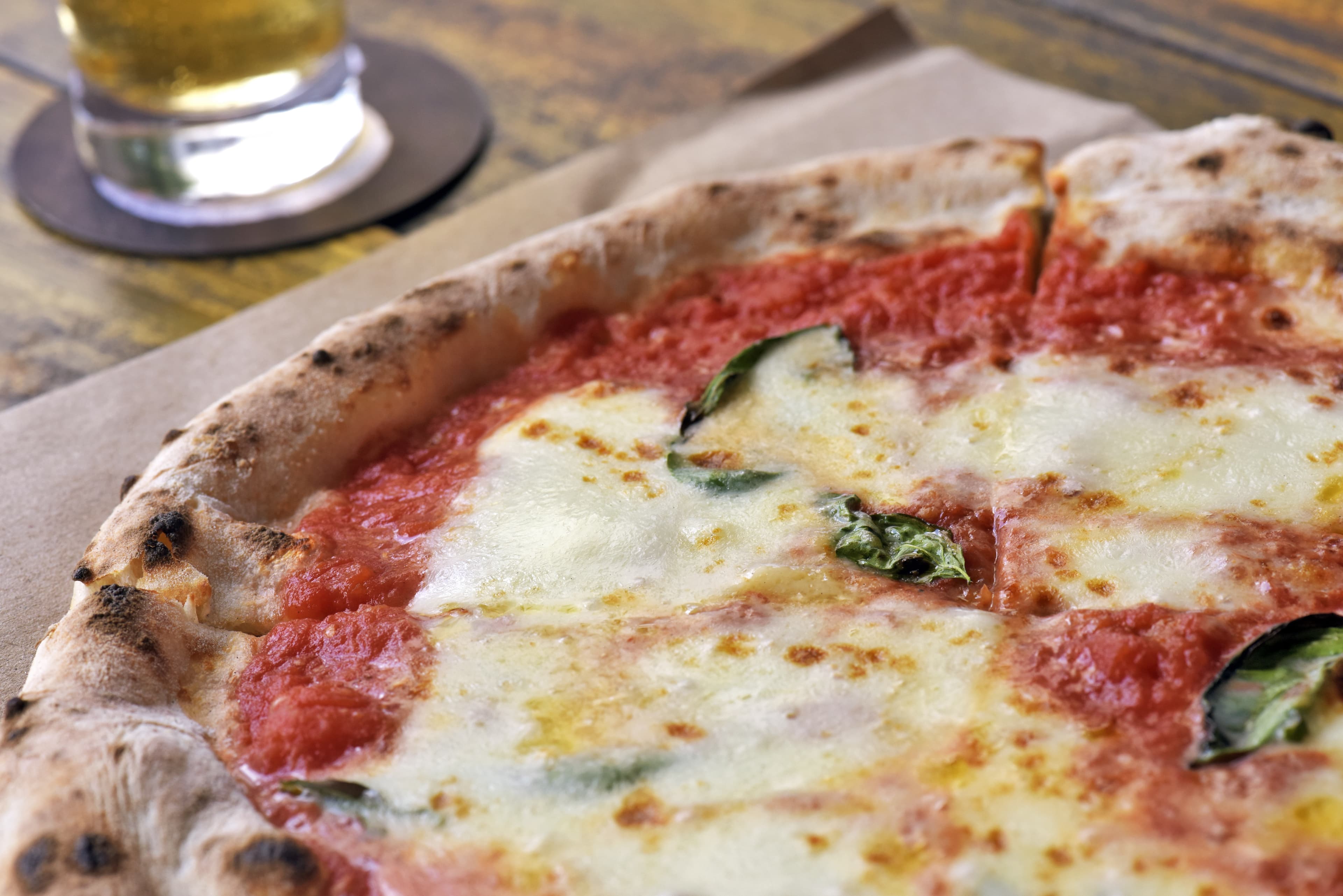 Pizza Margherita on a parchments paper on a old rustic wooden. Created in Naples with tomato sauce, mozzarella and basil. Today it is one of the culinary specialties of the city of Sao Paulo, Brazil Pizza Margherita on rustic wooden table