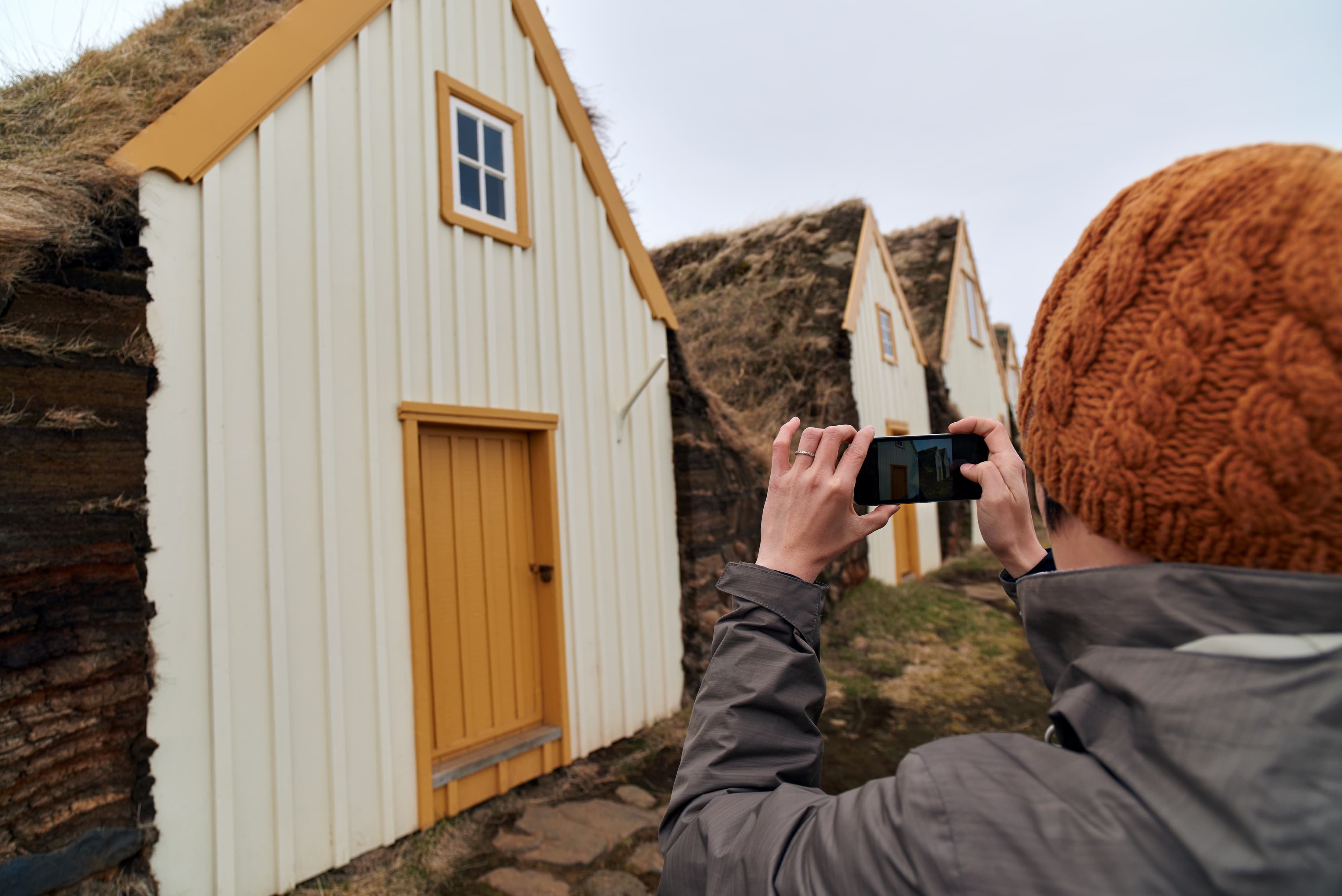 Woman taking picture with mobile cell phone of Traditional Icelandic Turf Houses in North Iceland Tourist taking picture of historic farmhouse