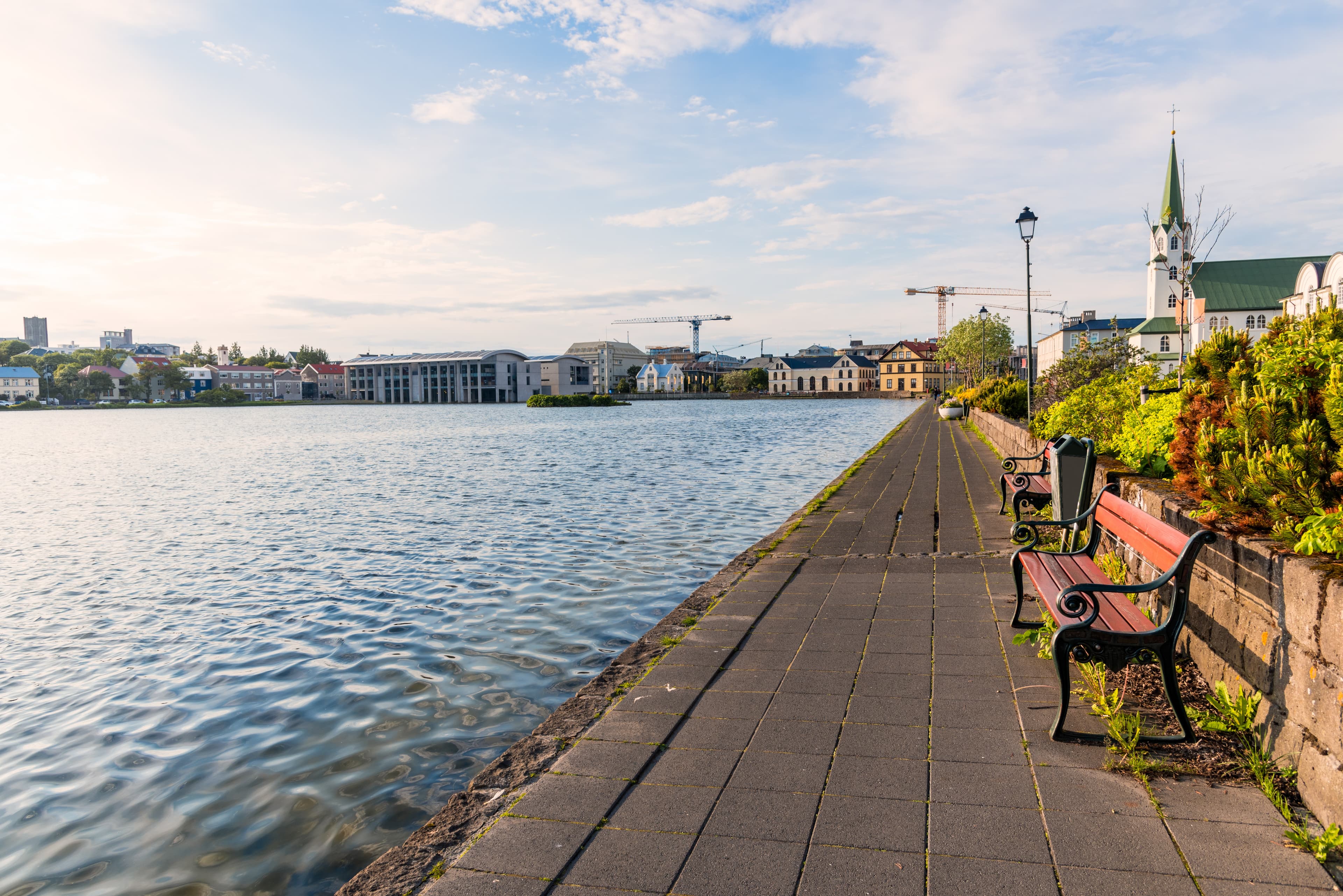 Footpath lined with empty wooden benches along the shore of a lake in a city centre. Reykjavik, Iceland. Footpath lined with empty wooden benches along the shore of a lake in a city centre. Reykjavik, Iceland.